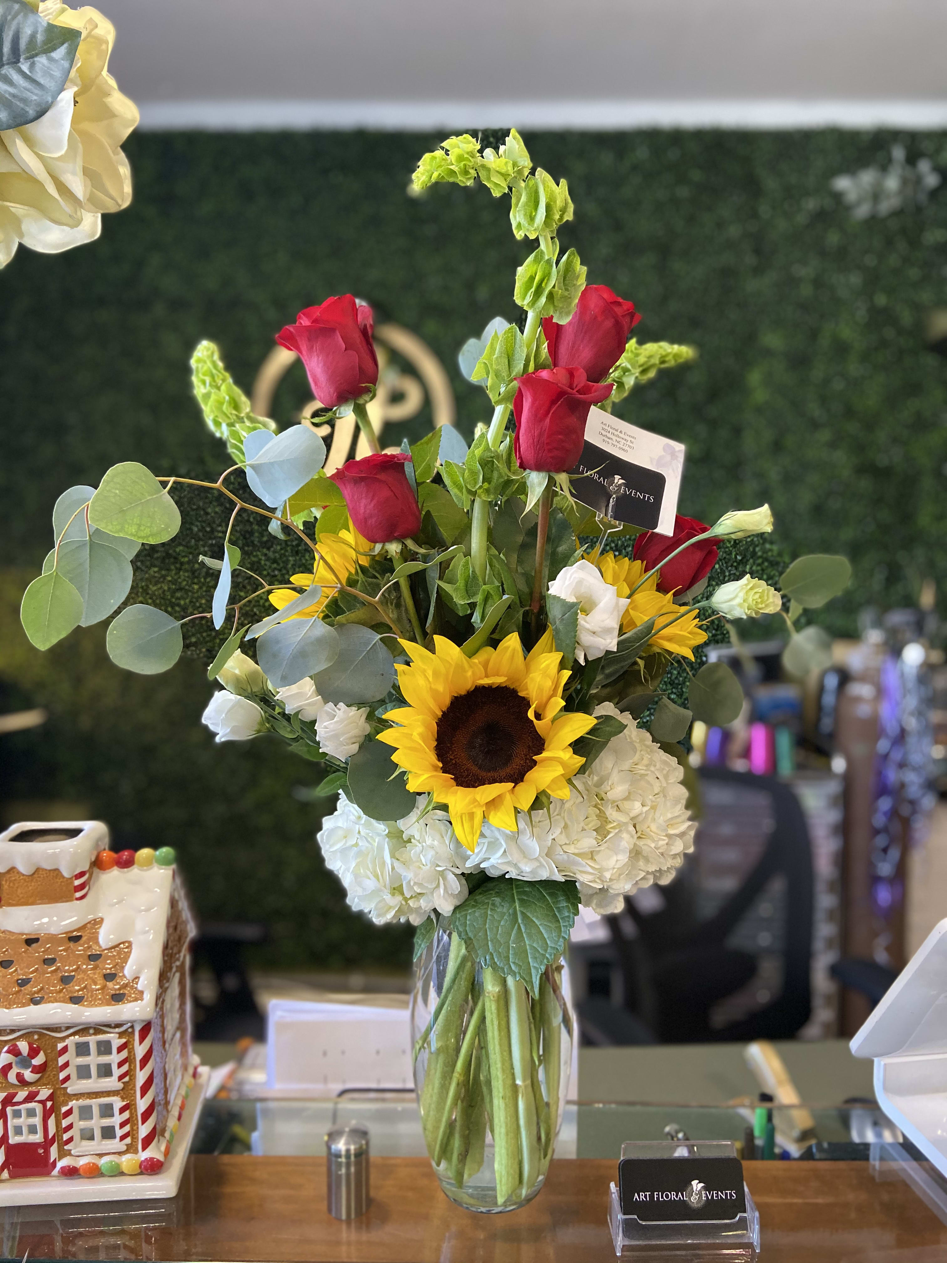 Mixed bouquet in a clear glass vase with red roses, a sunflower, and white hydrangeas.