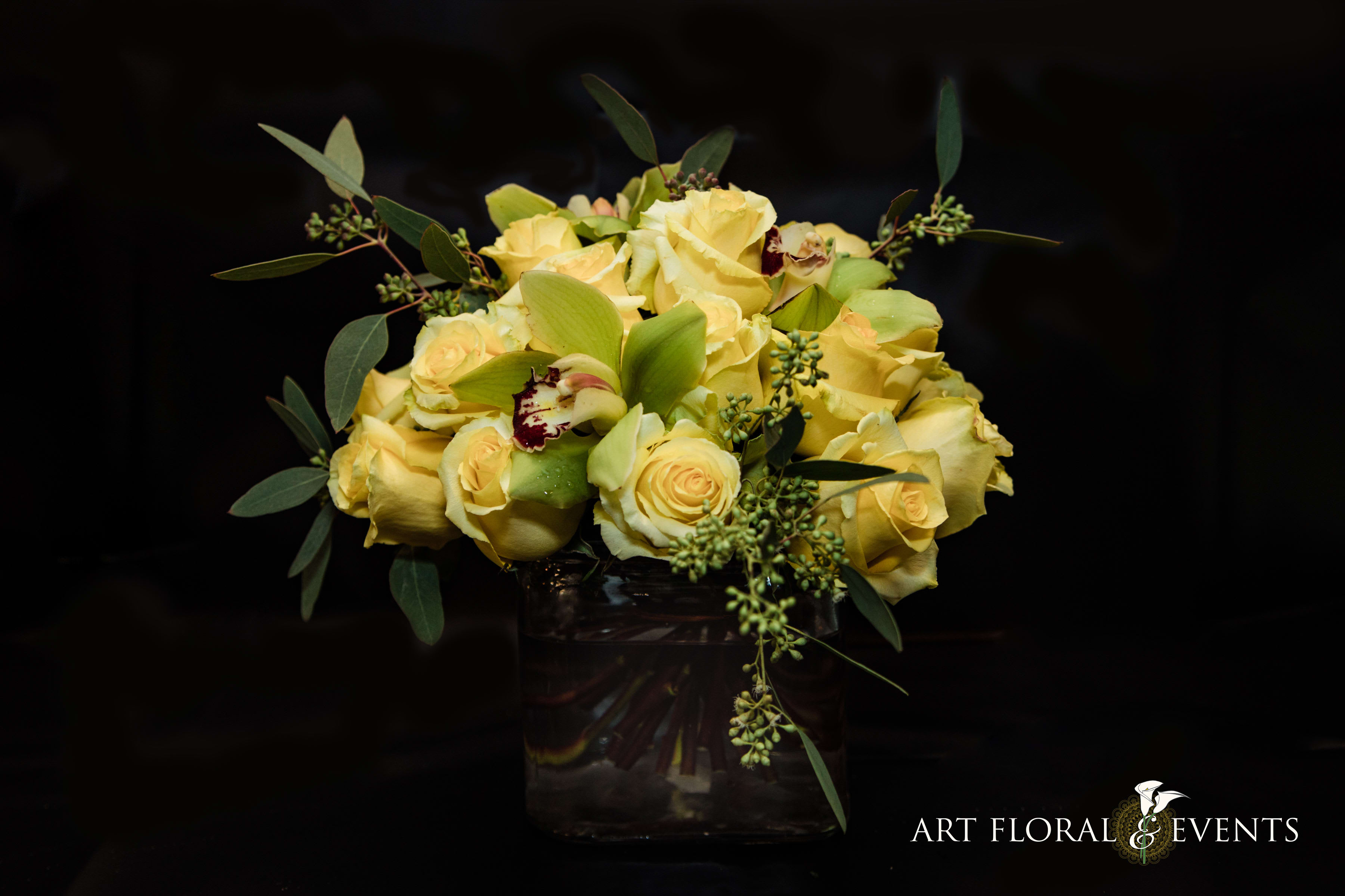 Yellow rose bouquet in a glass vase with green foliage