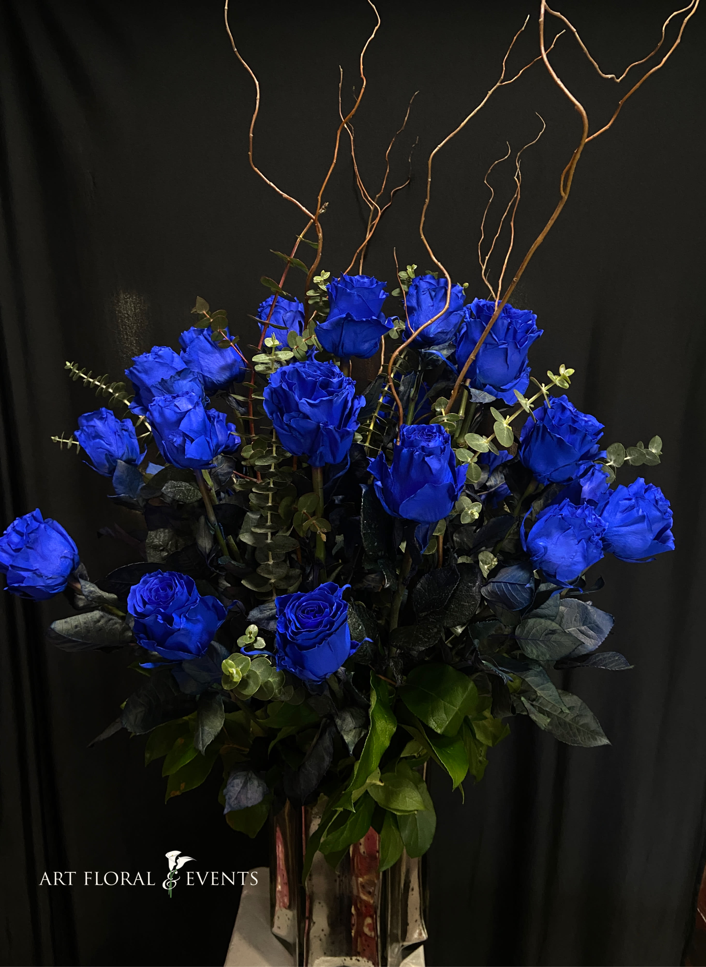 Arrangement of vivid blue roses in a tall vase with curly branches