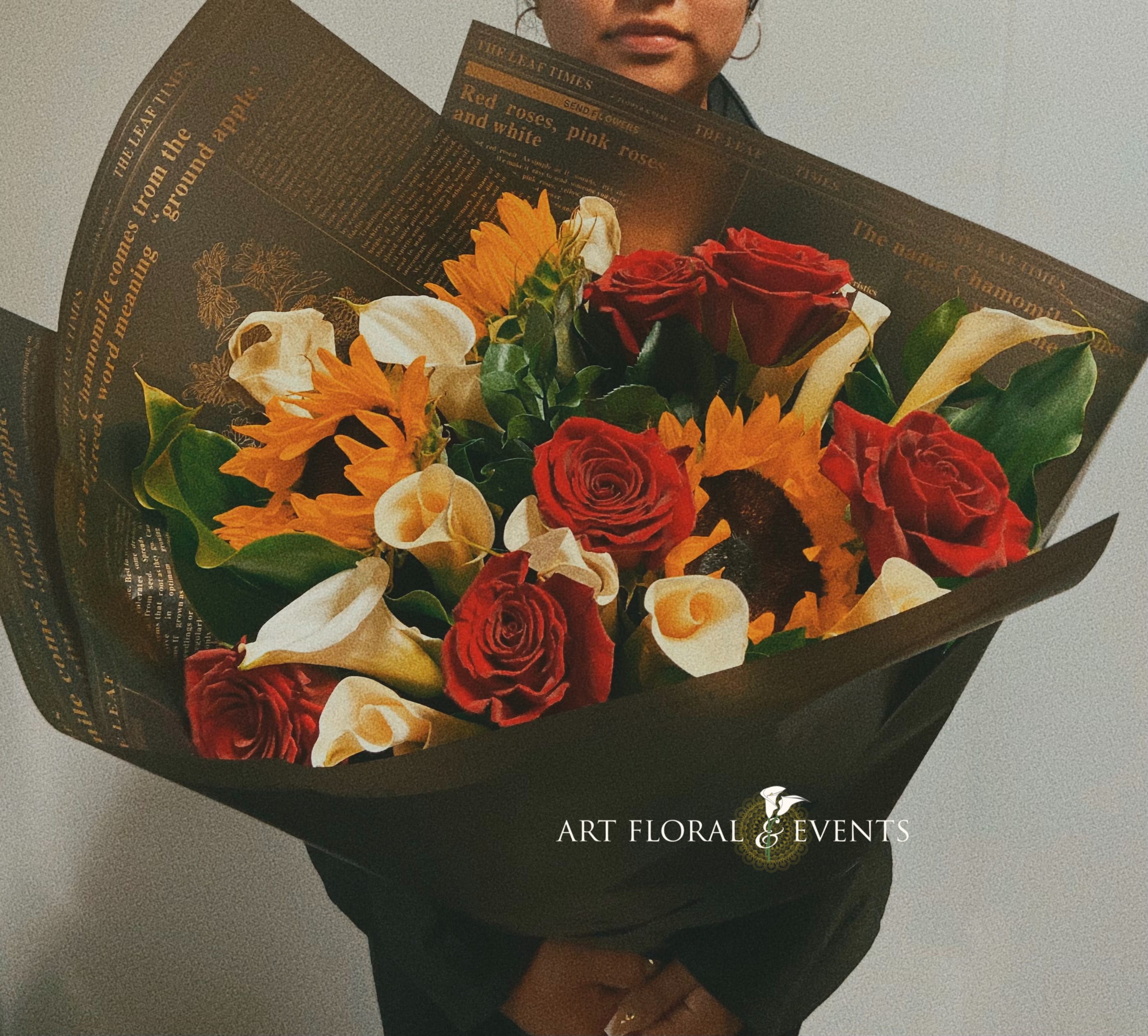 Bouquet of red roses, white calla lilies, and orange flowers wrapped in black paper