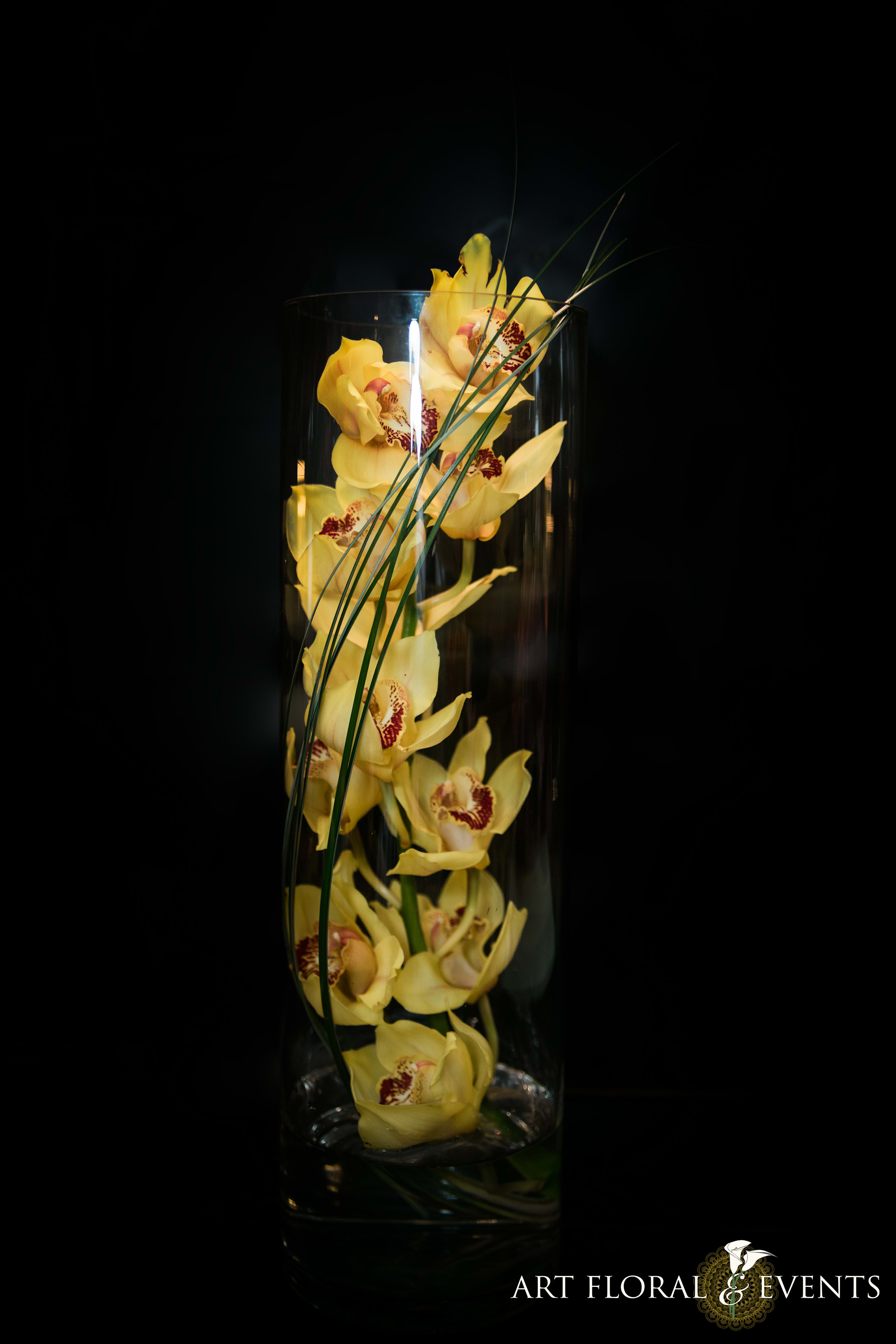 Yellow orchids arranged in a tall glass vase with long grass blades