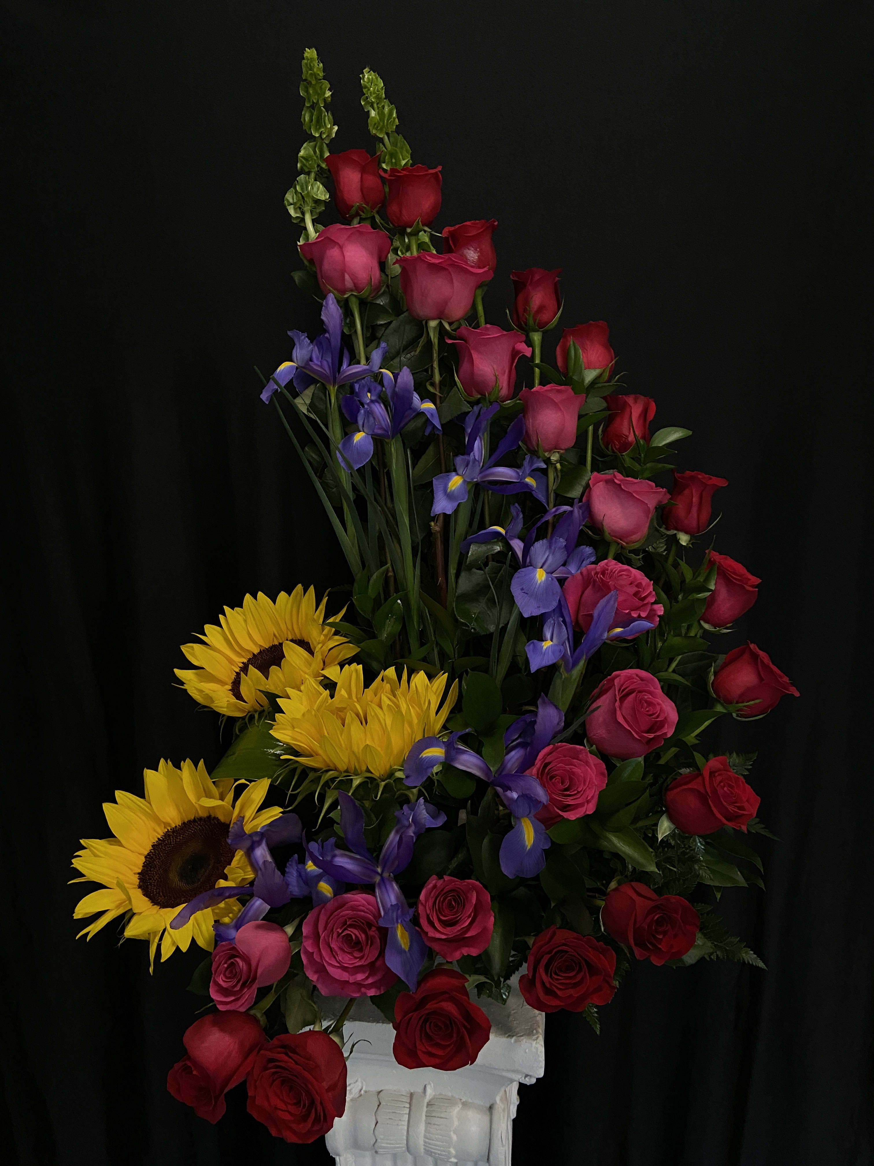 Tall arrangement of red and pink roses with purple irises and yellow sunflowers