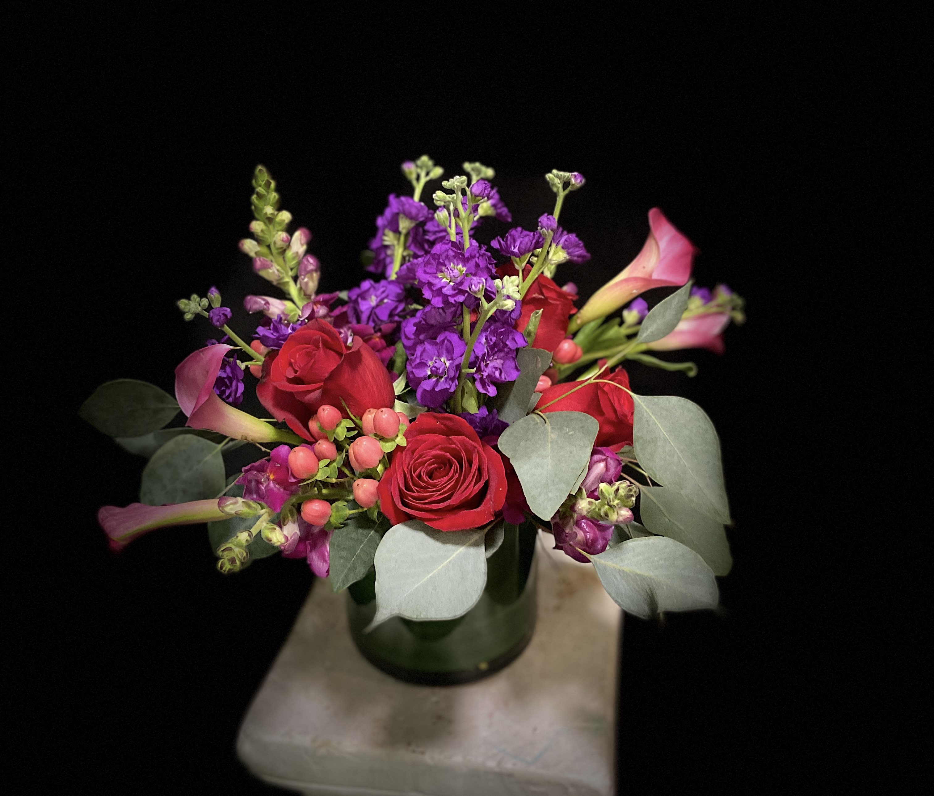 Bouquet of red roses, purple flowers, and pink calla lilies in a glass vase
