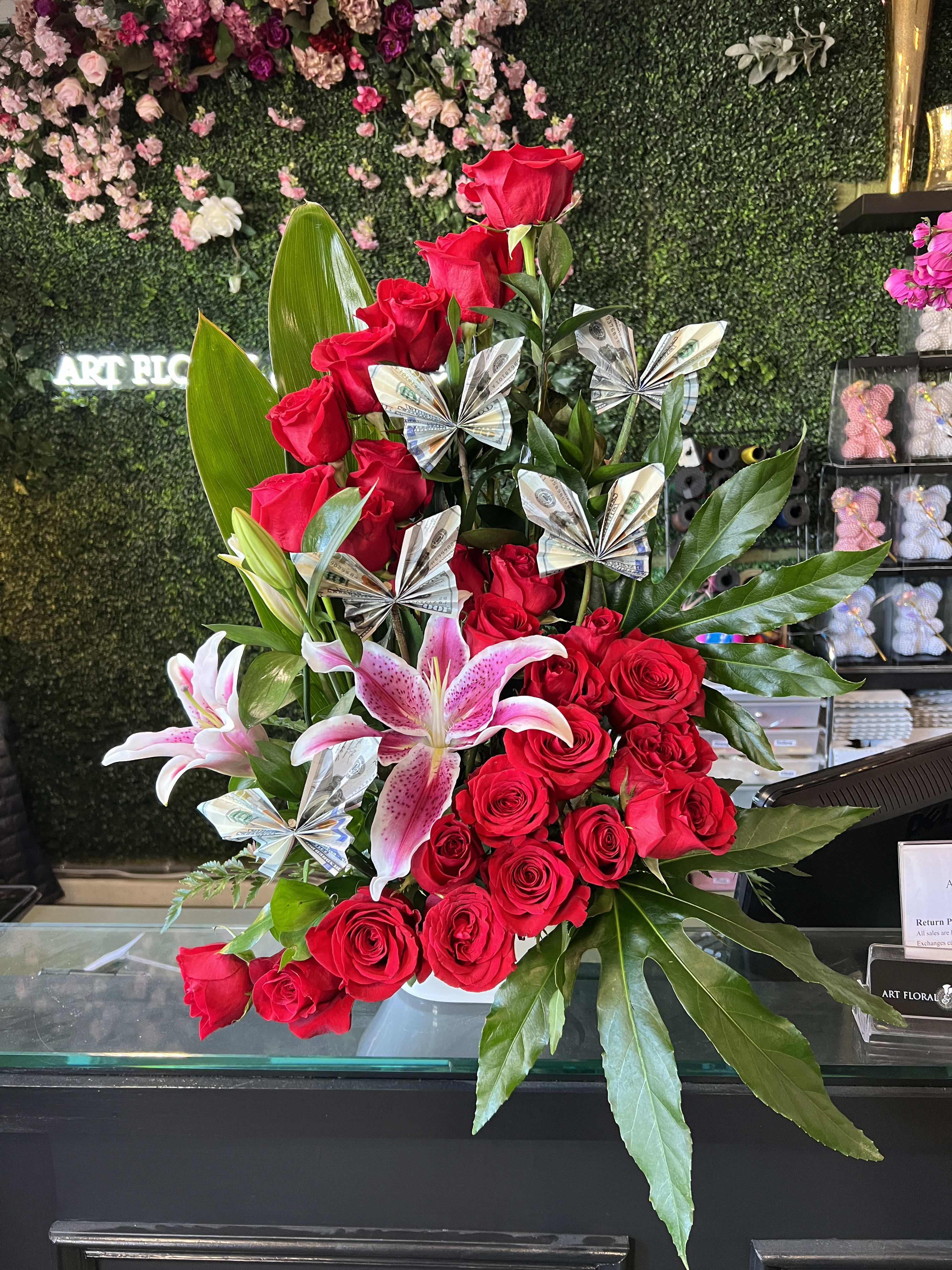 Red roses and pink lilies in a vase with folded money accents