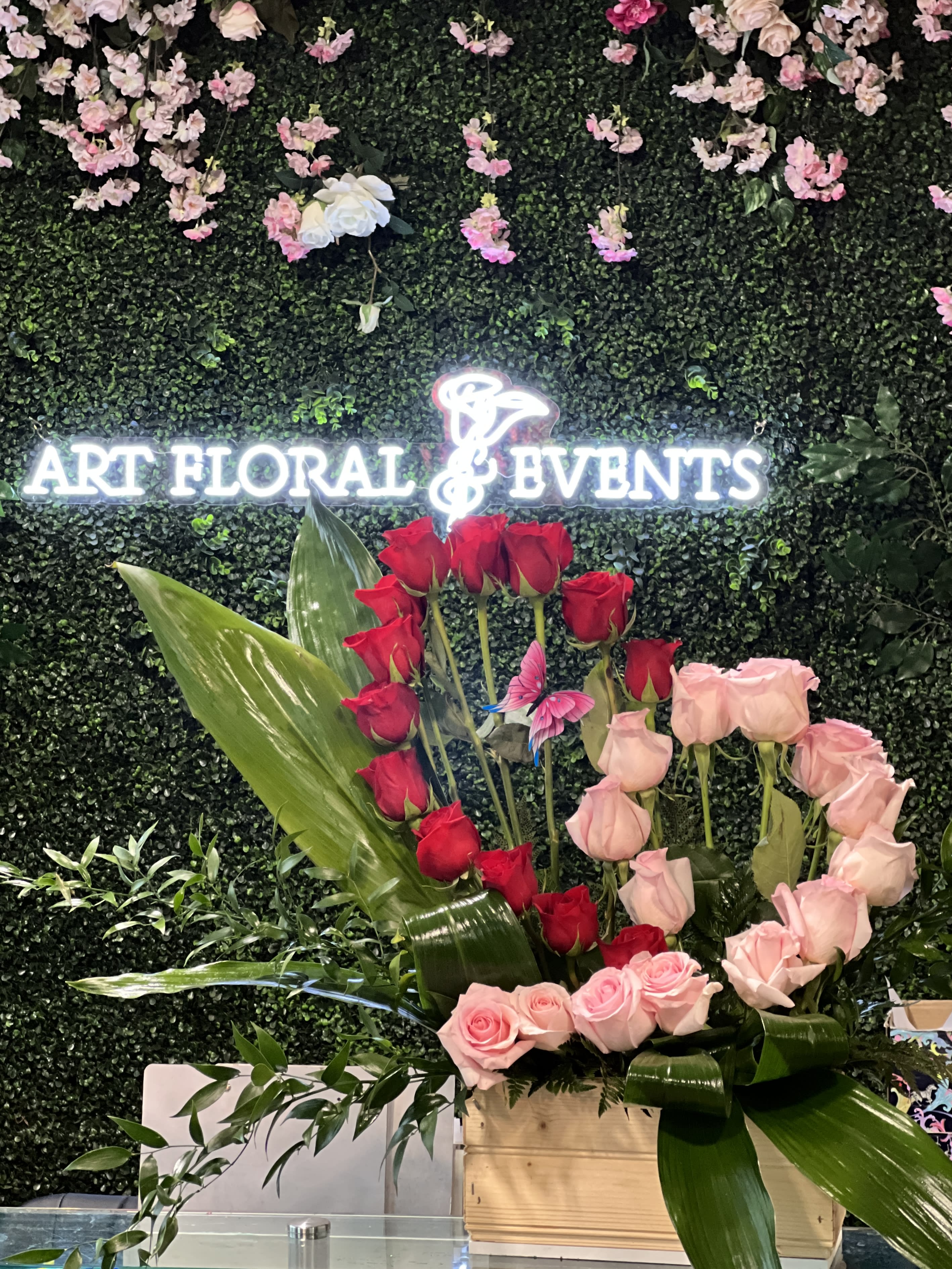 Red and pink roses arranged in a wooden box with large tropical leaves