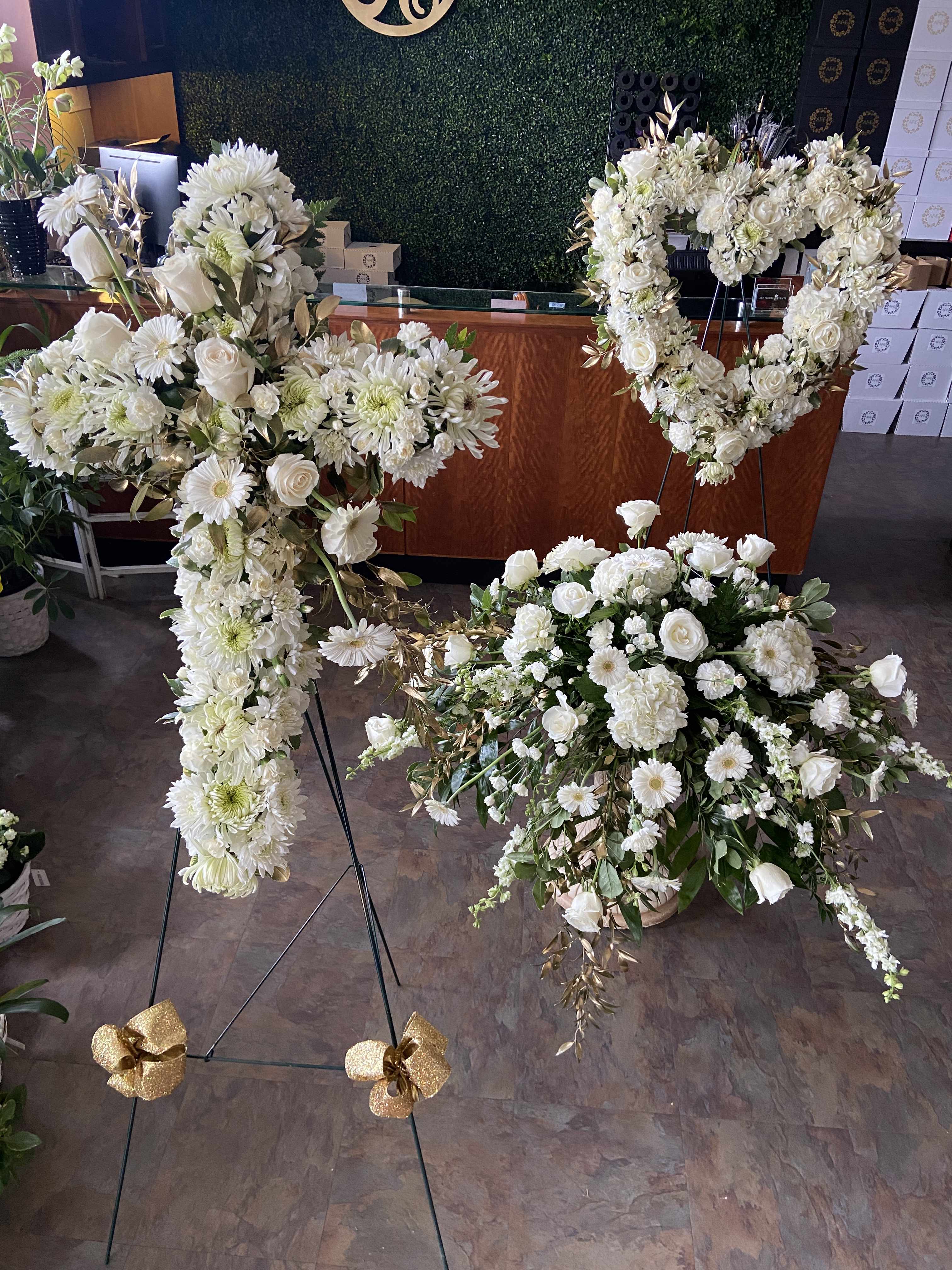 White floral funeral sprays and a heart-shaped wreath on stands