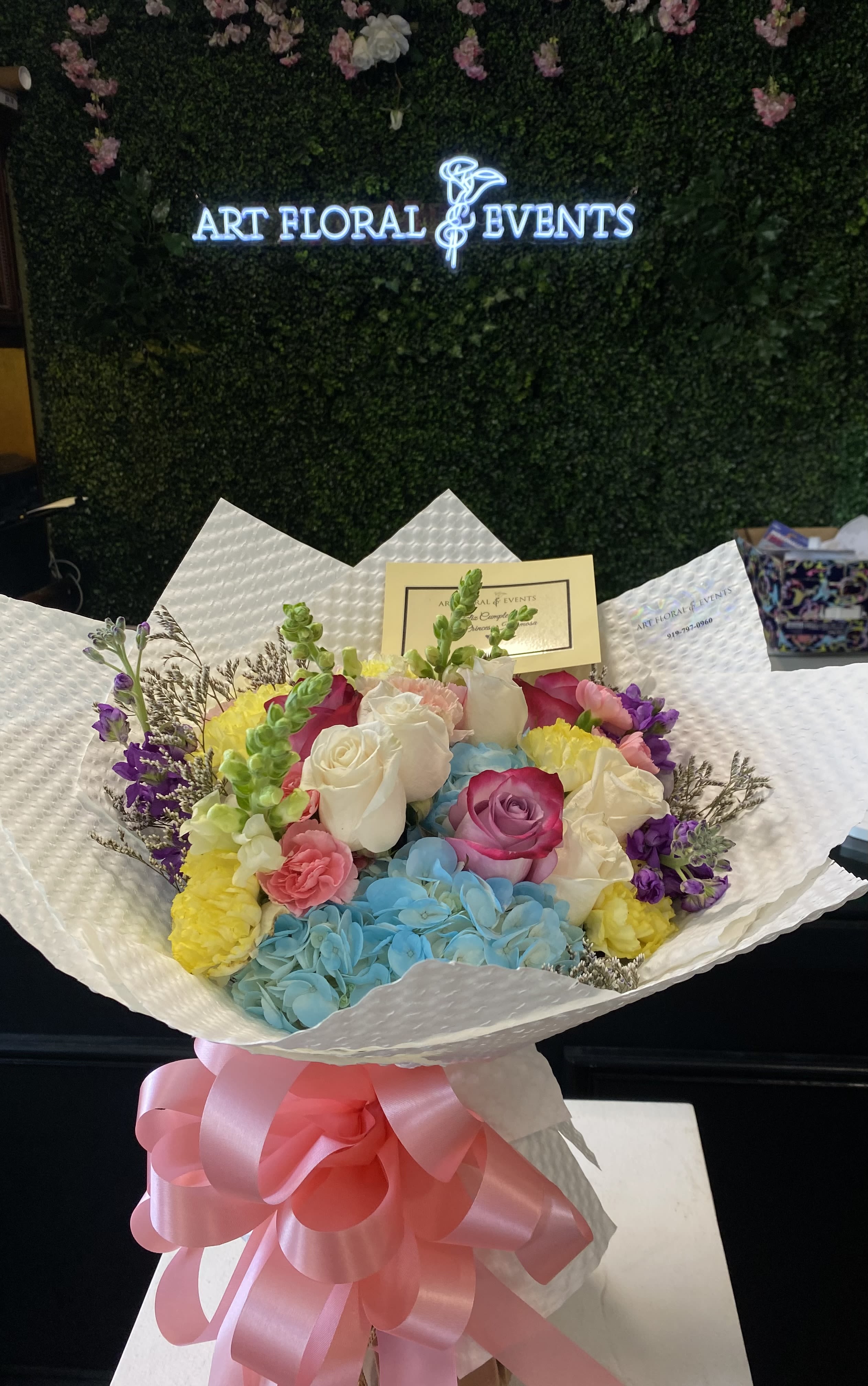 Colorful bouquet of roses, hydrangeas, and carnations wrapped in white paper with a pink bow