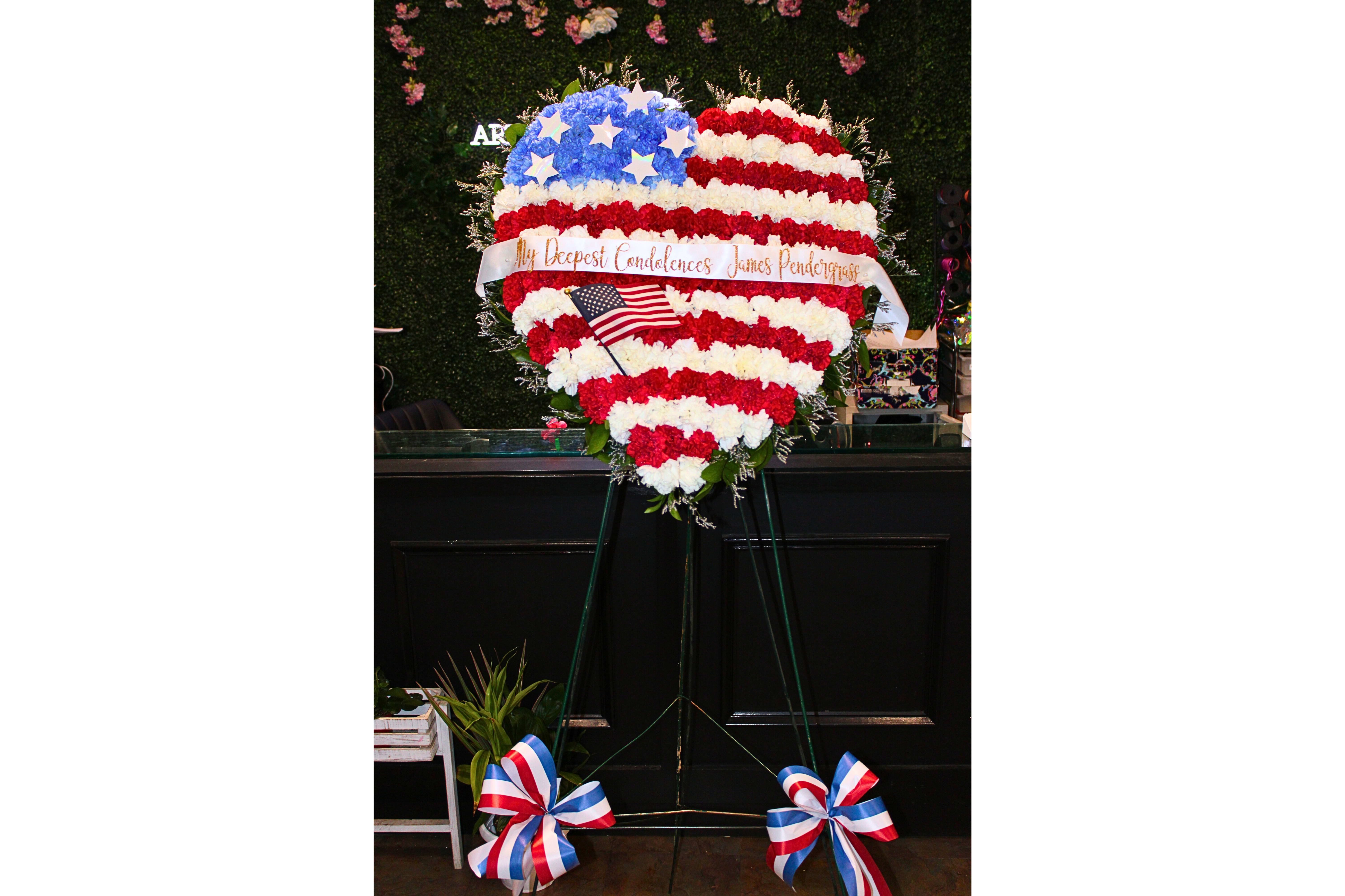 Heart-shaped red, white, and blue floral tribute on an easel with a ribbon