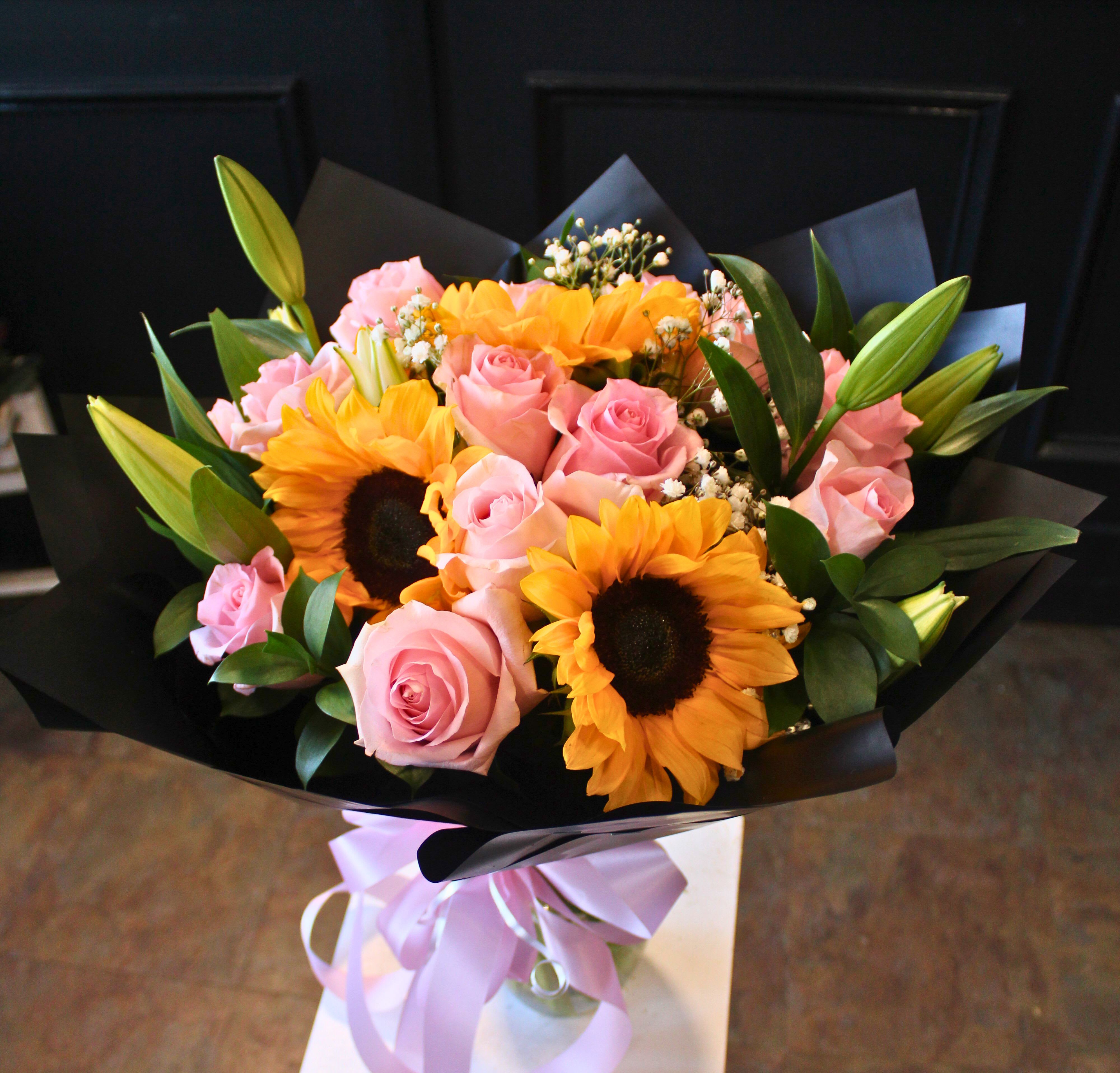 Bouquet of pink roses and sunflowers wrapped in black paper with a lavender ribbon
