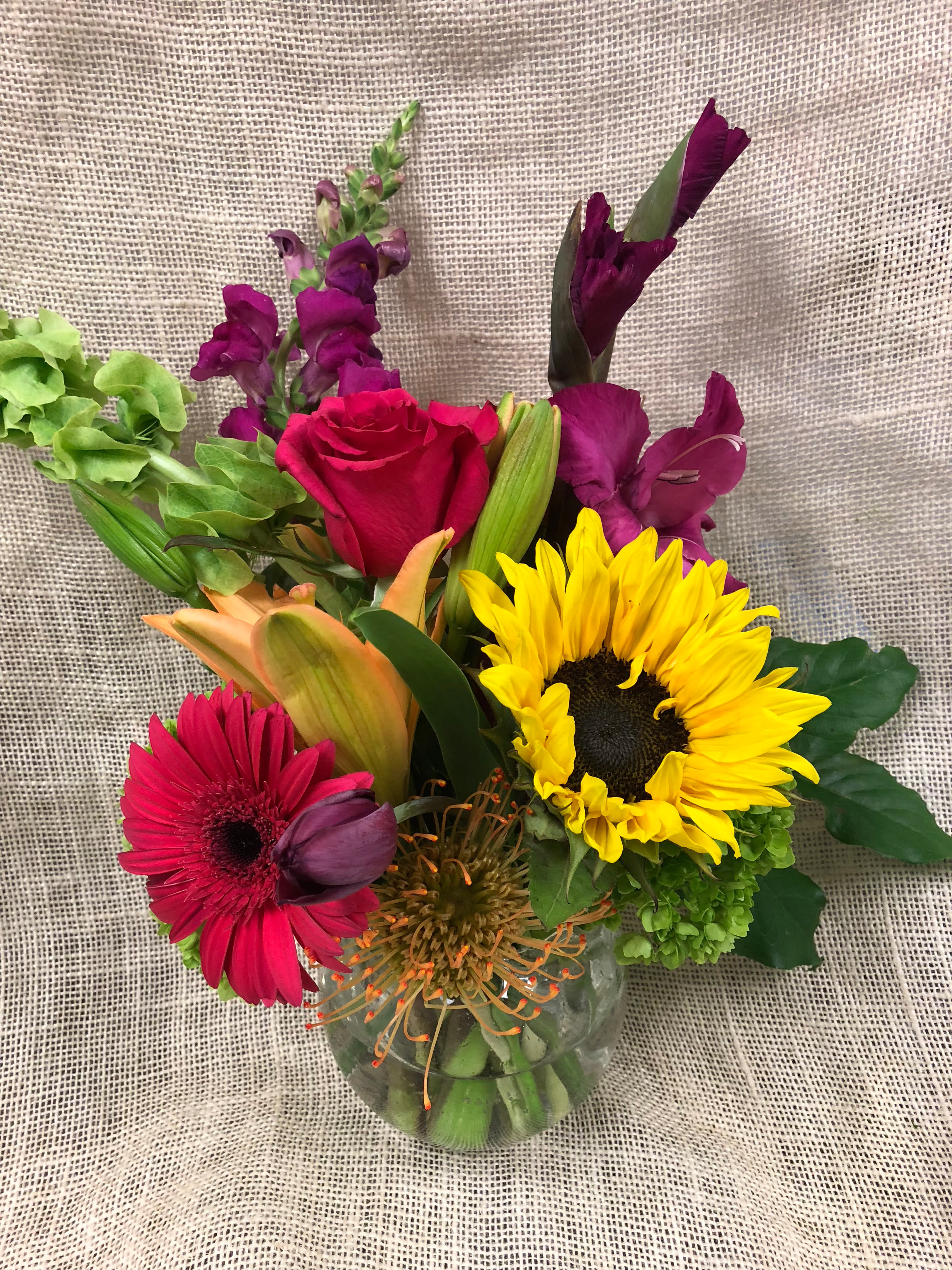 Mixed bouquet in a clear glass vase with a sunflower, rose, and gerbera daisies