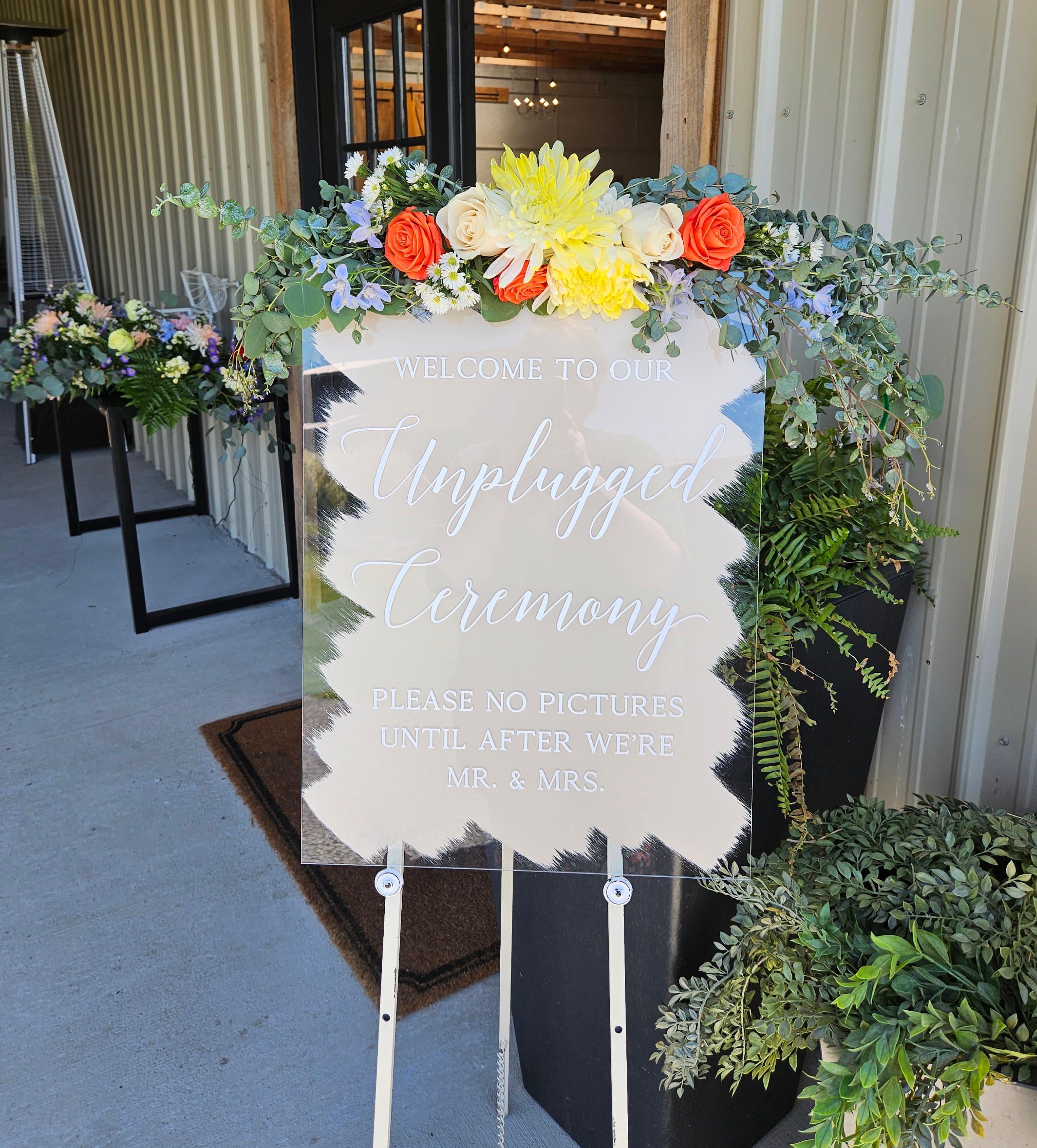 Floral sign topper with orange and yellow blooms and trailing greenery