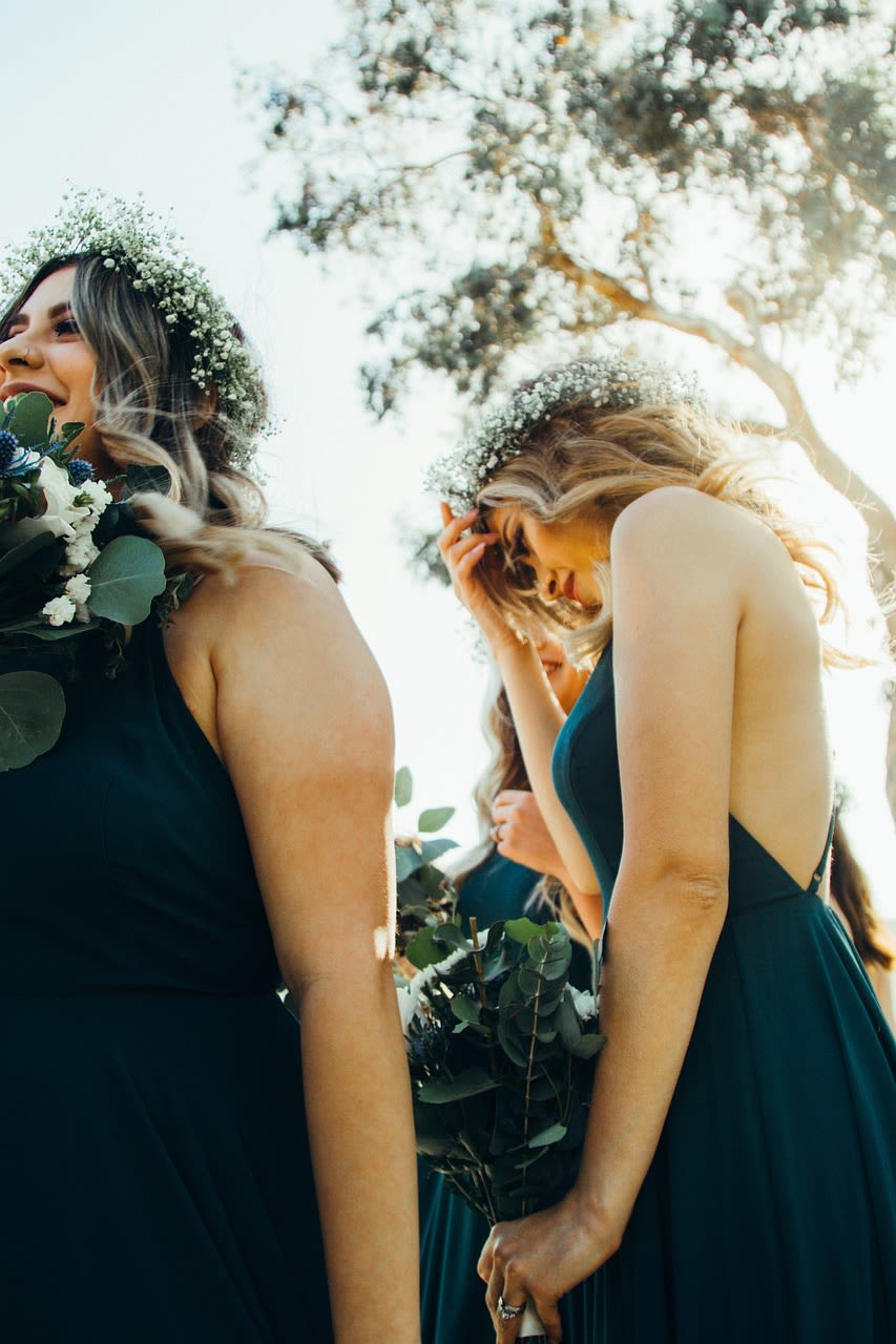 Bridesmaids in dark dresses holding bouquets and floral crowns outdoors