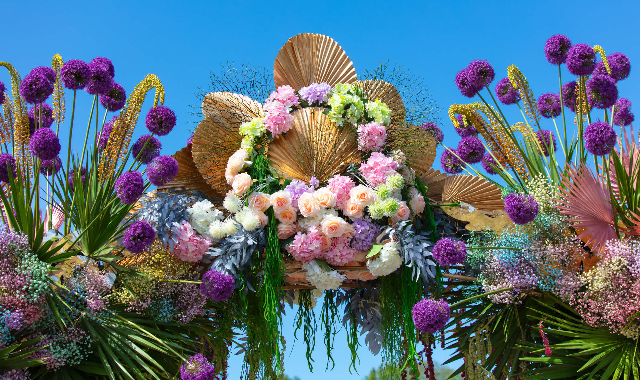 Large floral display with pink and white roses, purple allium-like blooms, and gold fan decorations