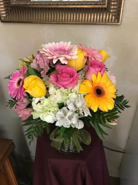 Pink and yellow roses with gerbera daisies in a glass vase