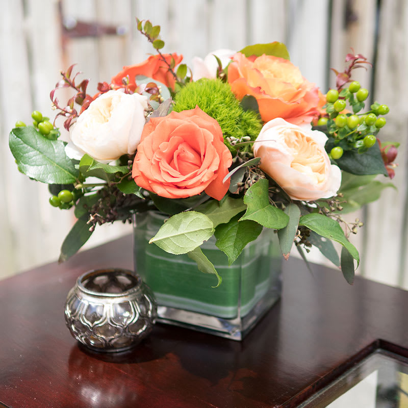 Pretty in cream and orange: Roses and other blossoms - Perfect balance of creams and peachy orange roses and other beautiful and lasting blossoms designed in glass vase with leaf wrap. Starting size is designed in 5" cube, overall floral canopy spanning approximately 10" across.