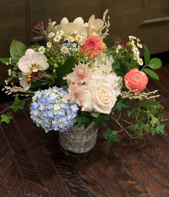 Mixed bouquet in a gray vase with orchids, roses, hydrangea, and small daisies