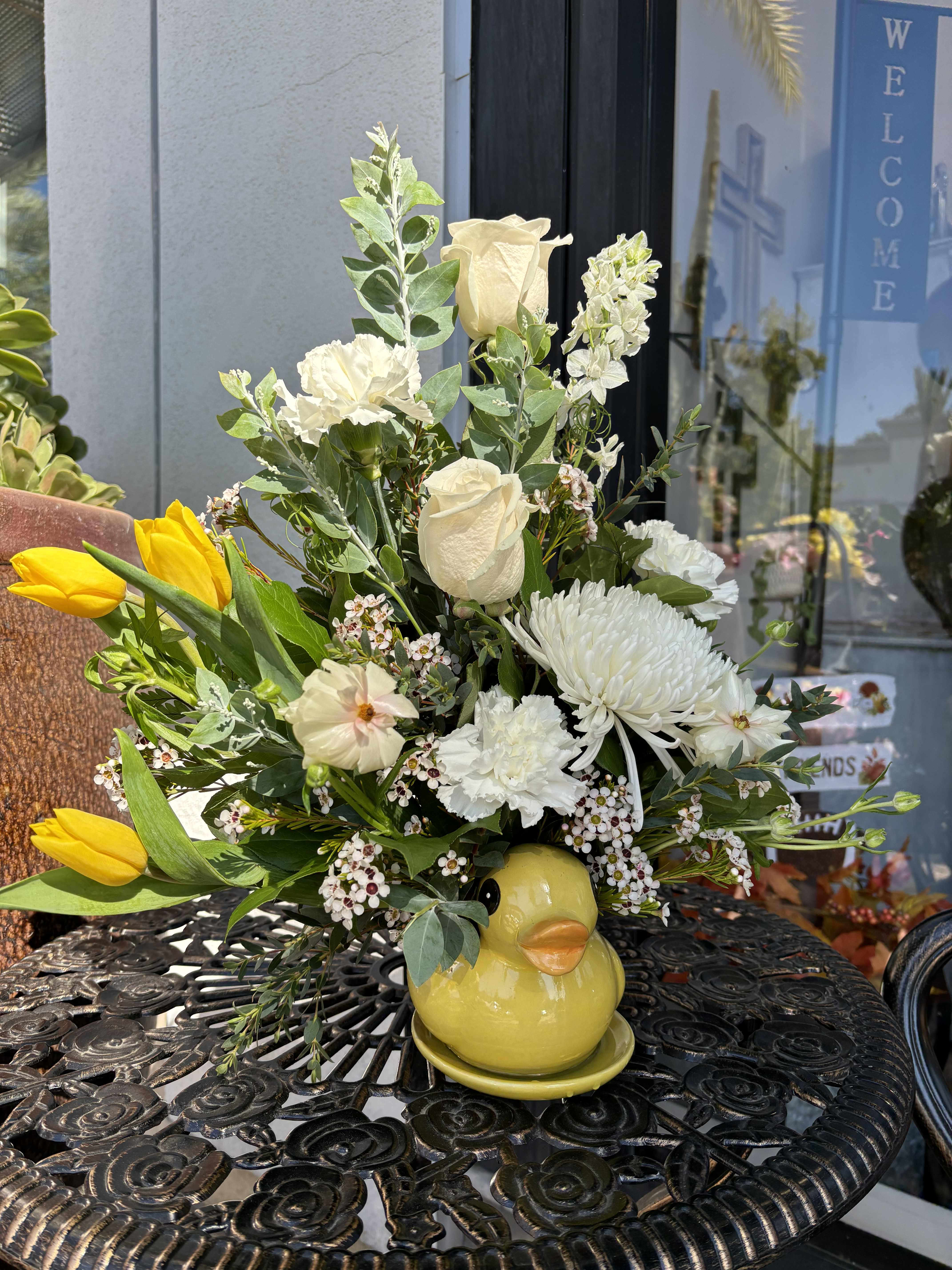 Bouquet of white flowers and yellow tulips in a yellow duck vase