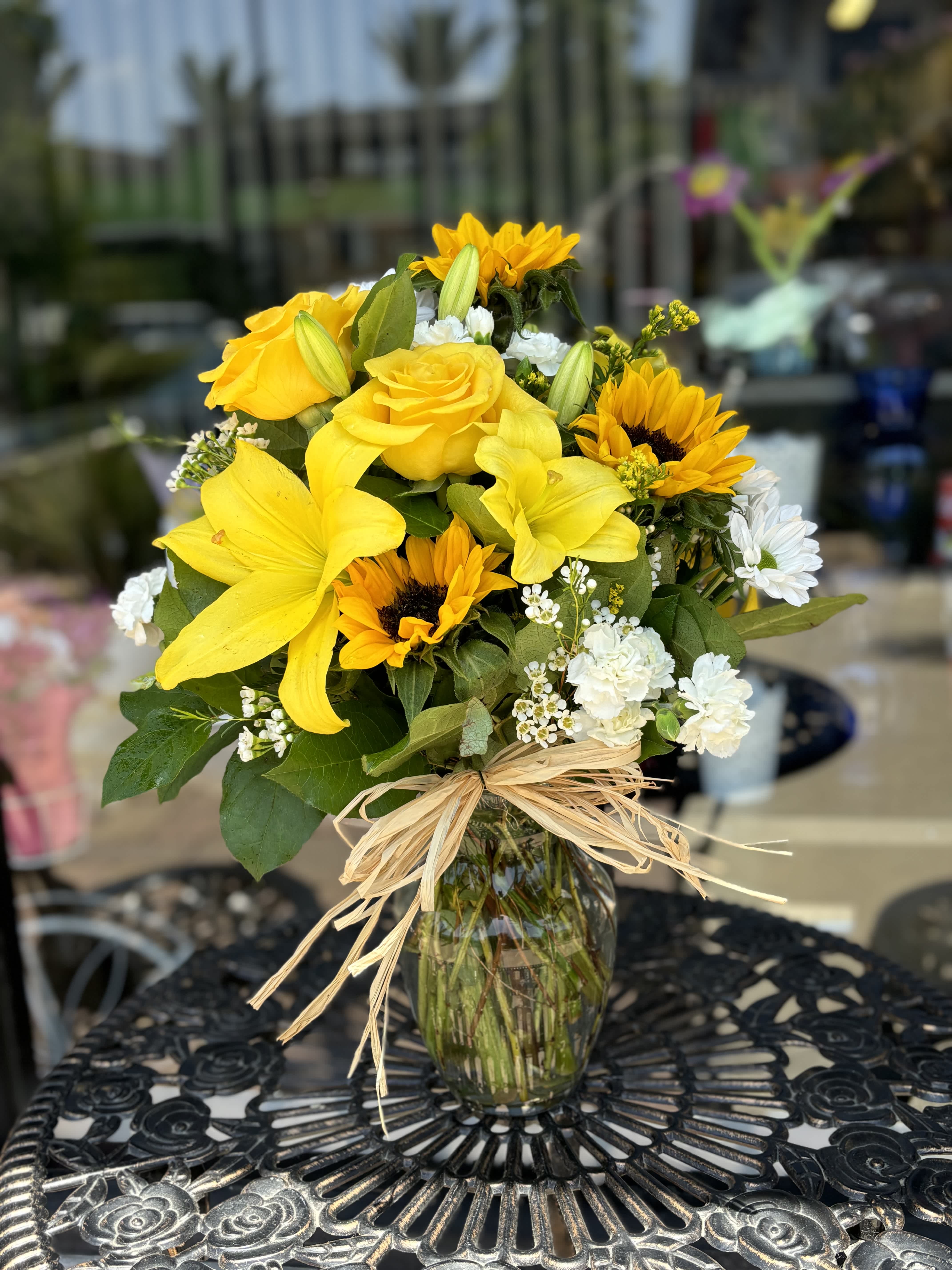Yellow bouquet with sunflowers, roses, and white flowers in a glass vase