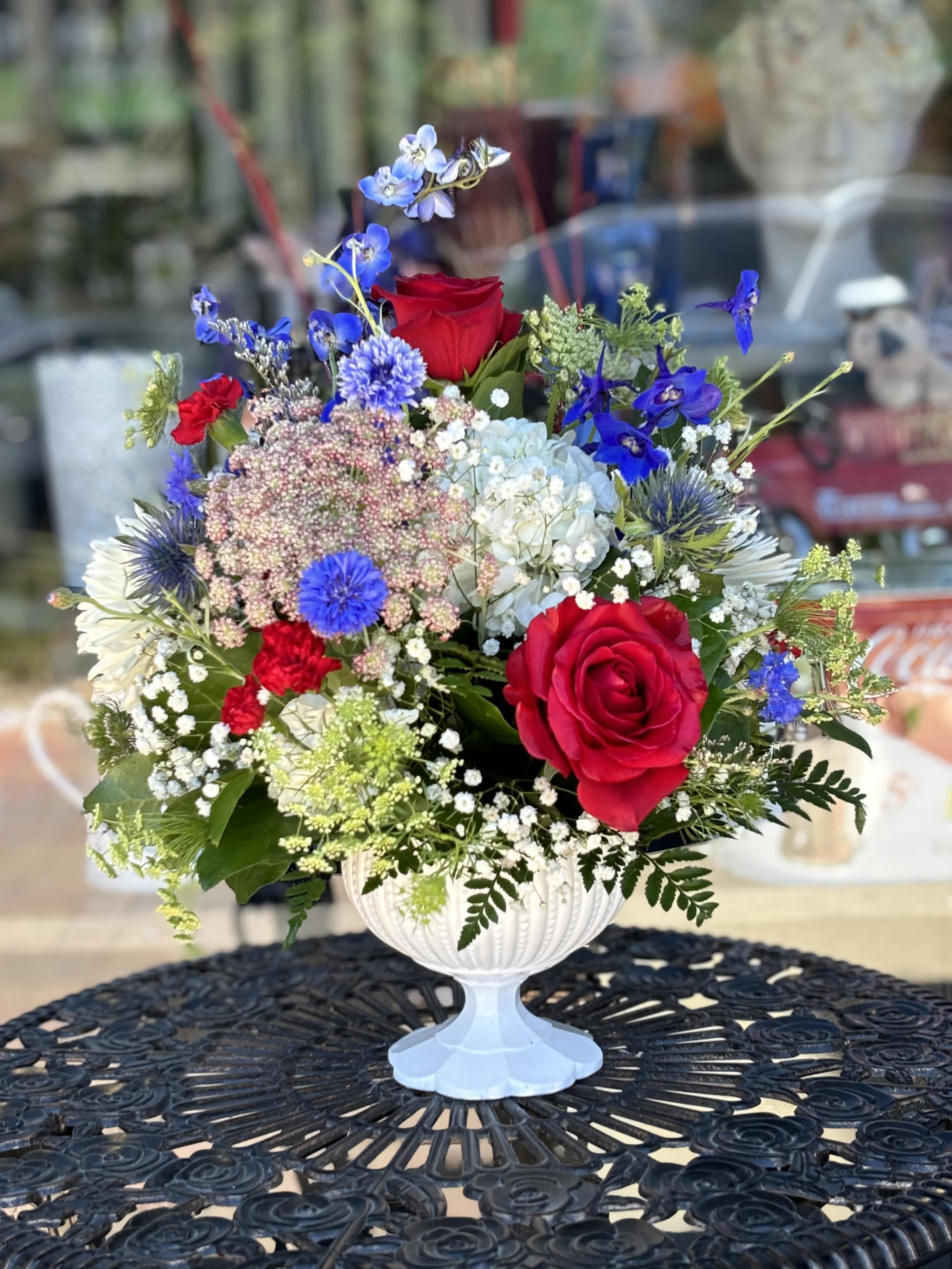 Mixed bouquet of red roses and blue flowers in a white pedestal vase