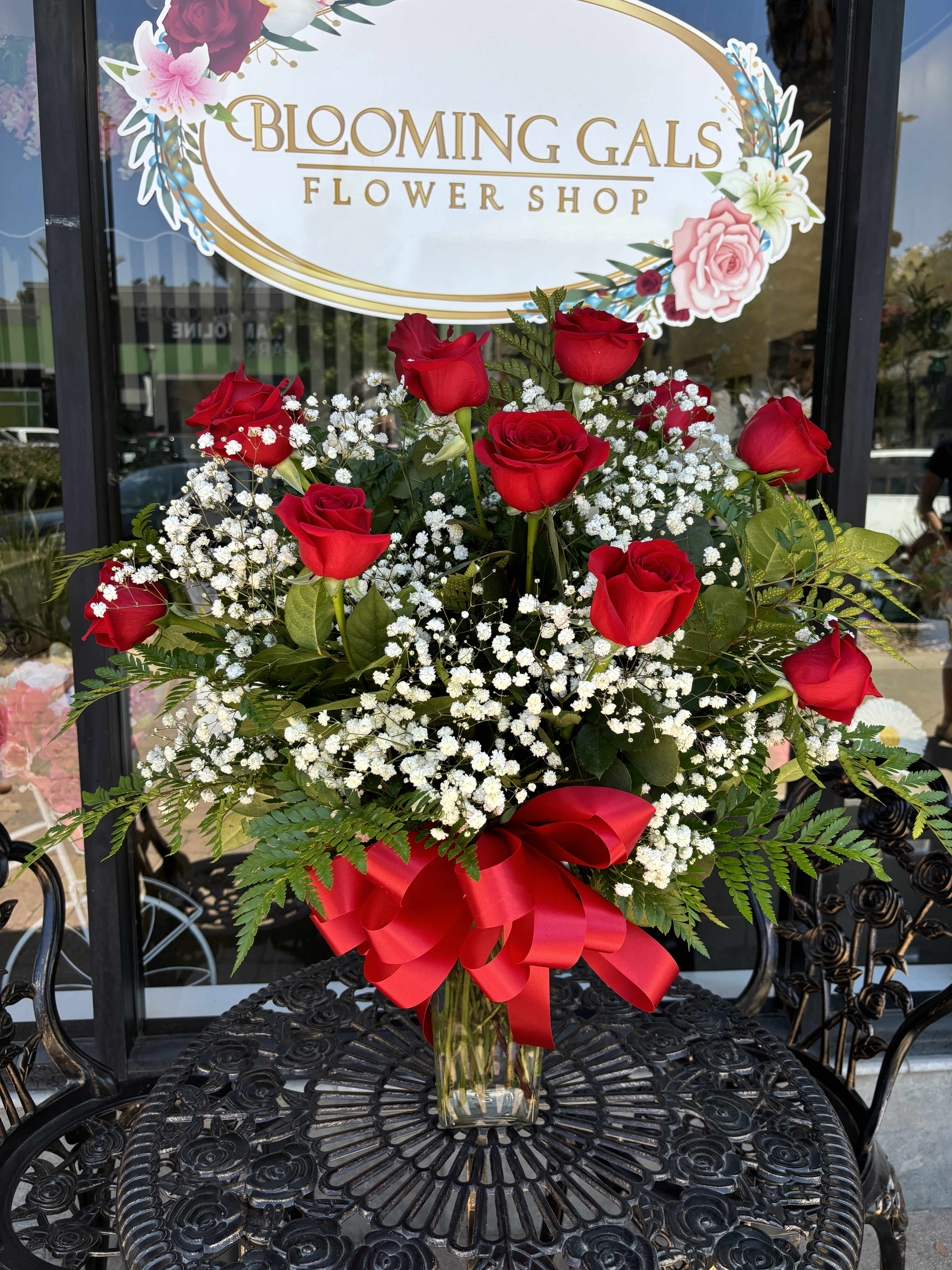 Red roses and baby's breath in a clear glass vase with a red ribbon