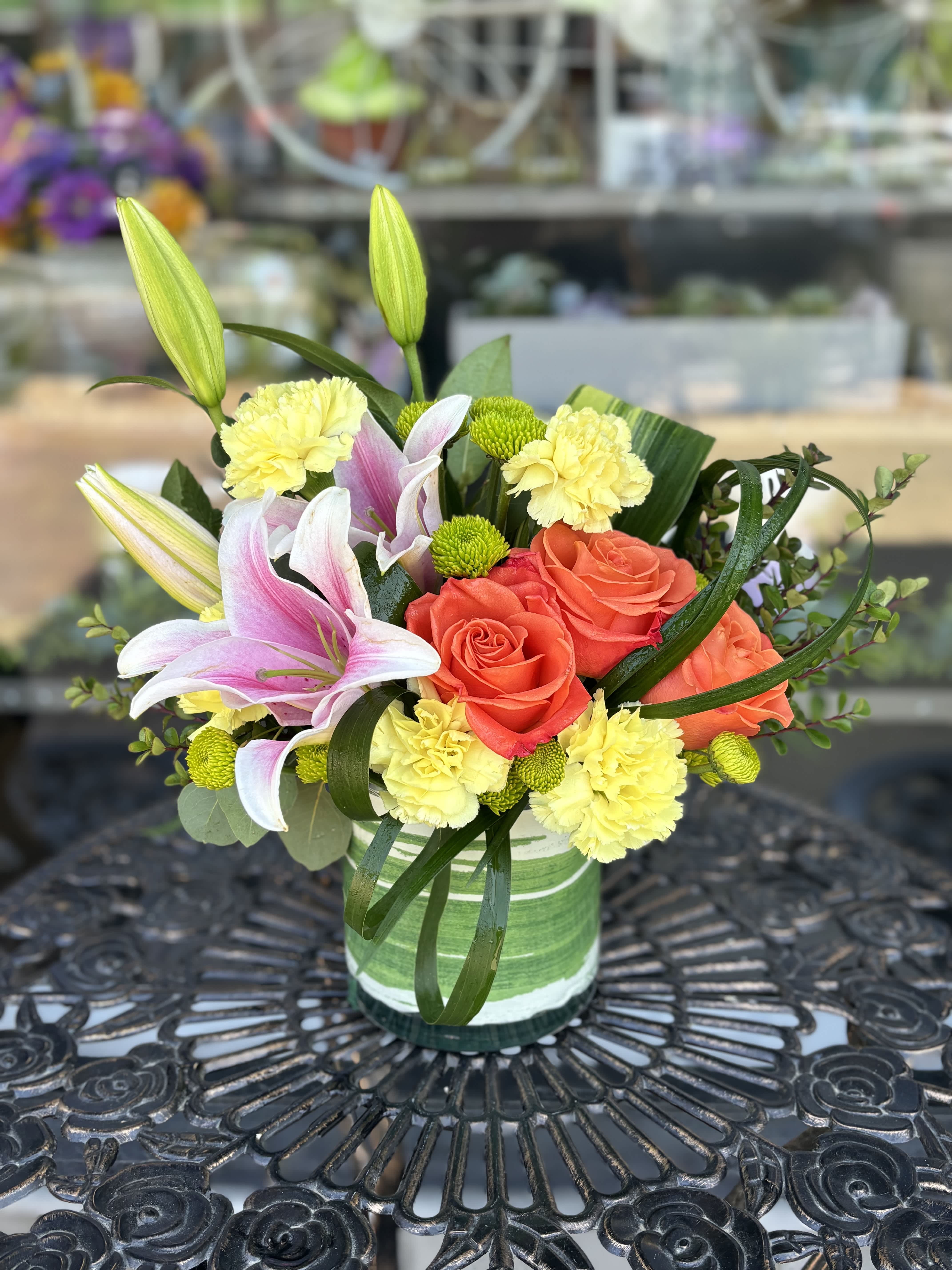 Bouquet of pink lilies, coral roses, and yellow carnations in a glass vase