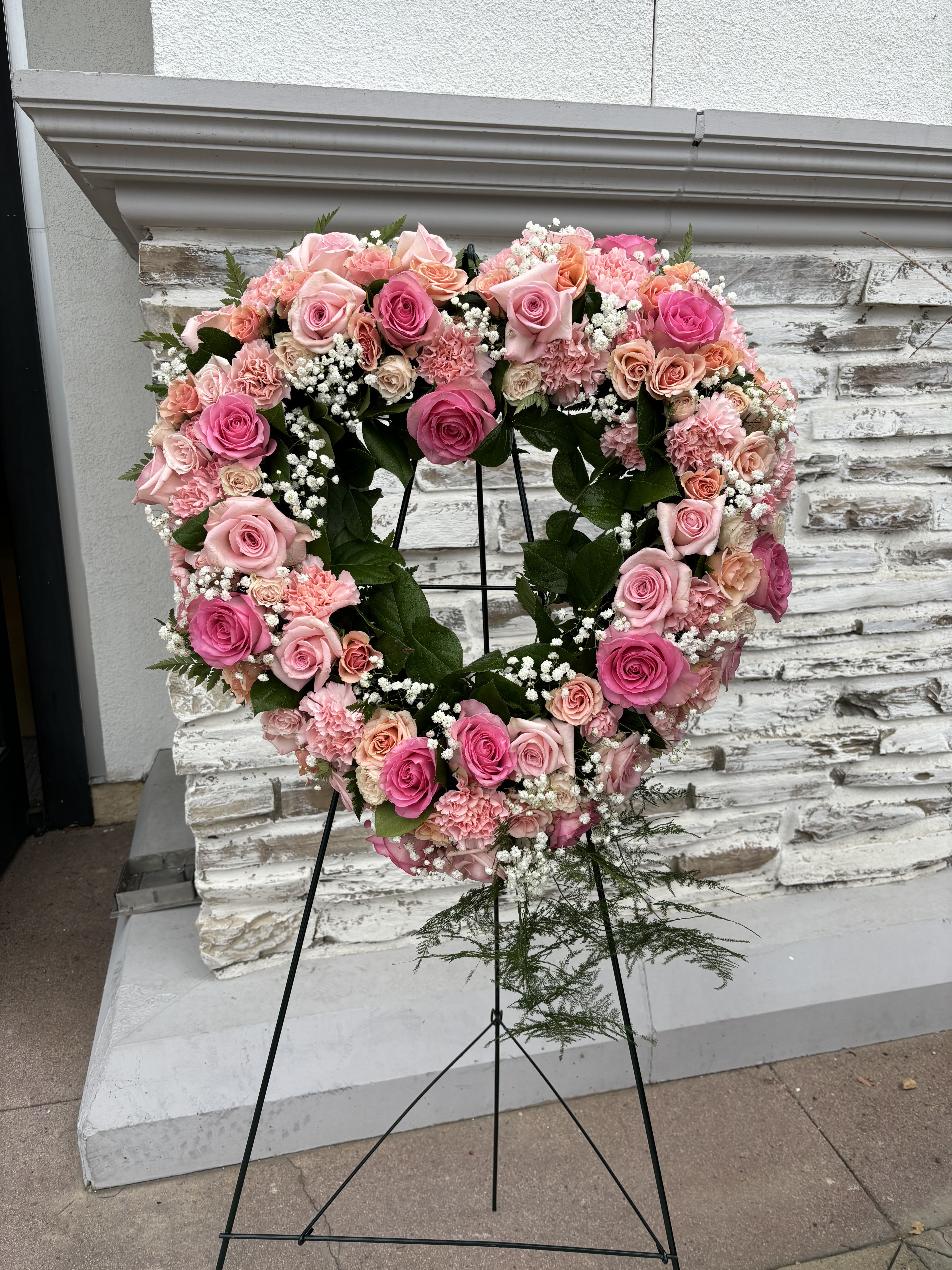 Heart-shaped floral wreath of pink roses and carnations on a stand