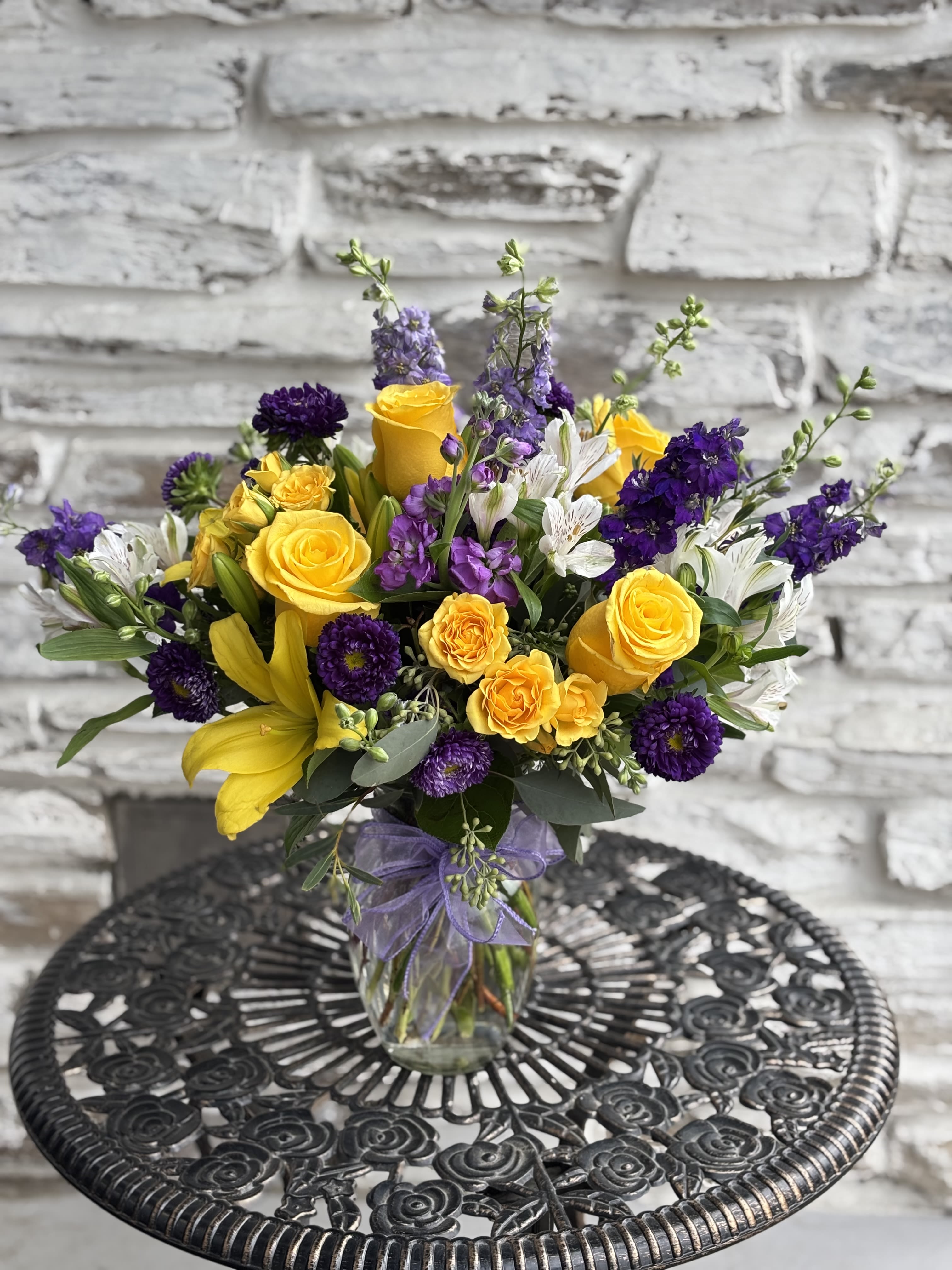 Bouquet of yellow roses, purple flowers, and white lilies in a glass vase