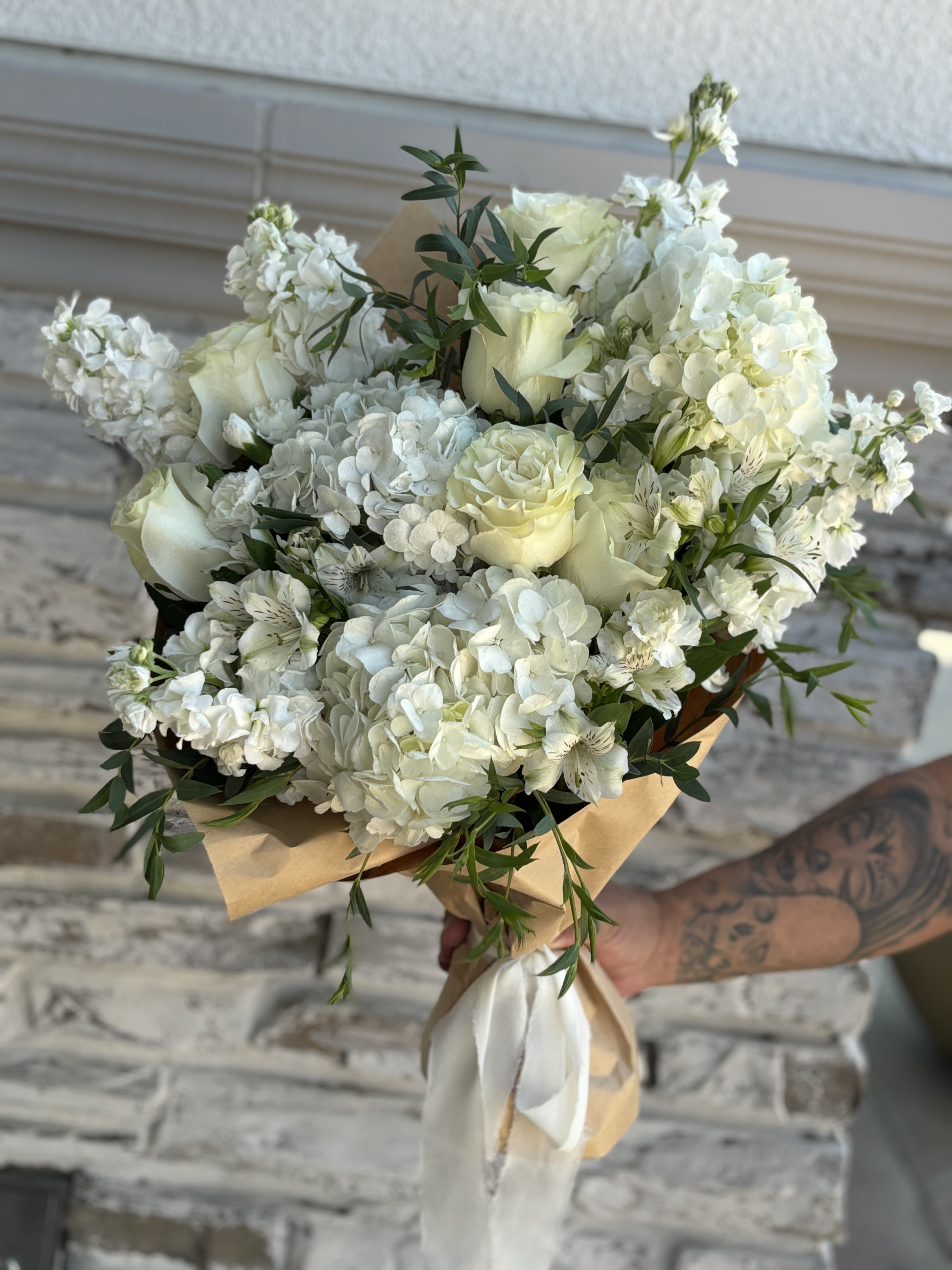 White rose and hydrangea bouquet wrapped in tan paper with a white ribbon