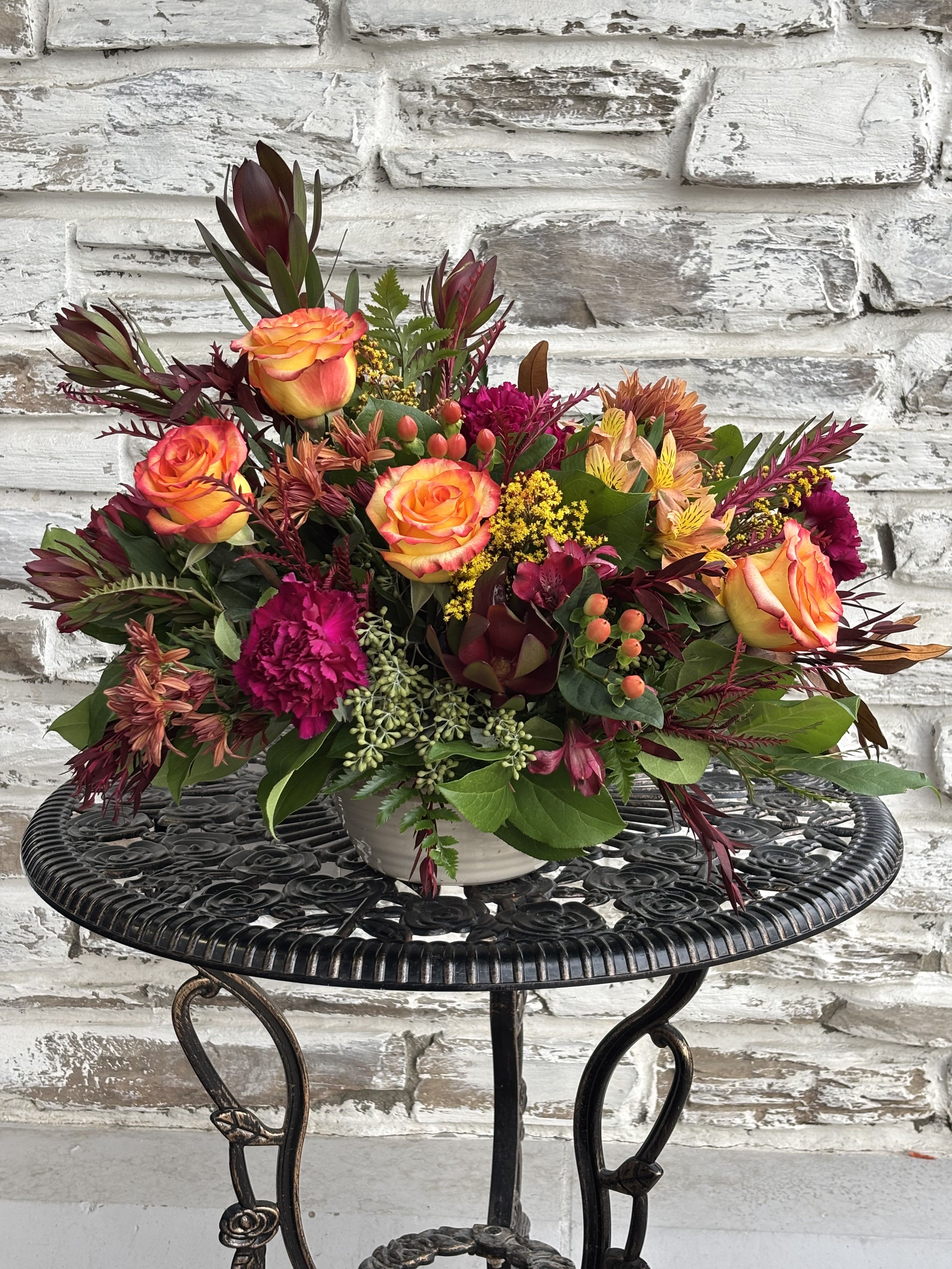 Mixed bouquet of orange roses and magenta flowers in a white vase
