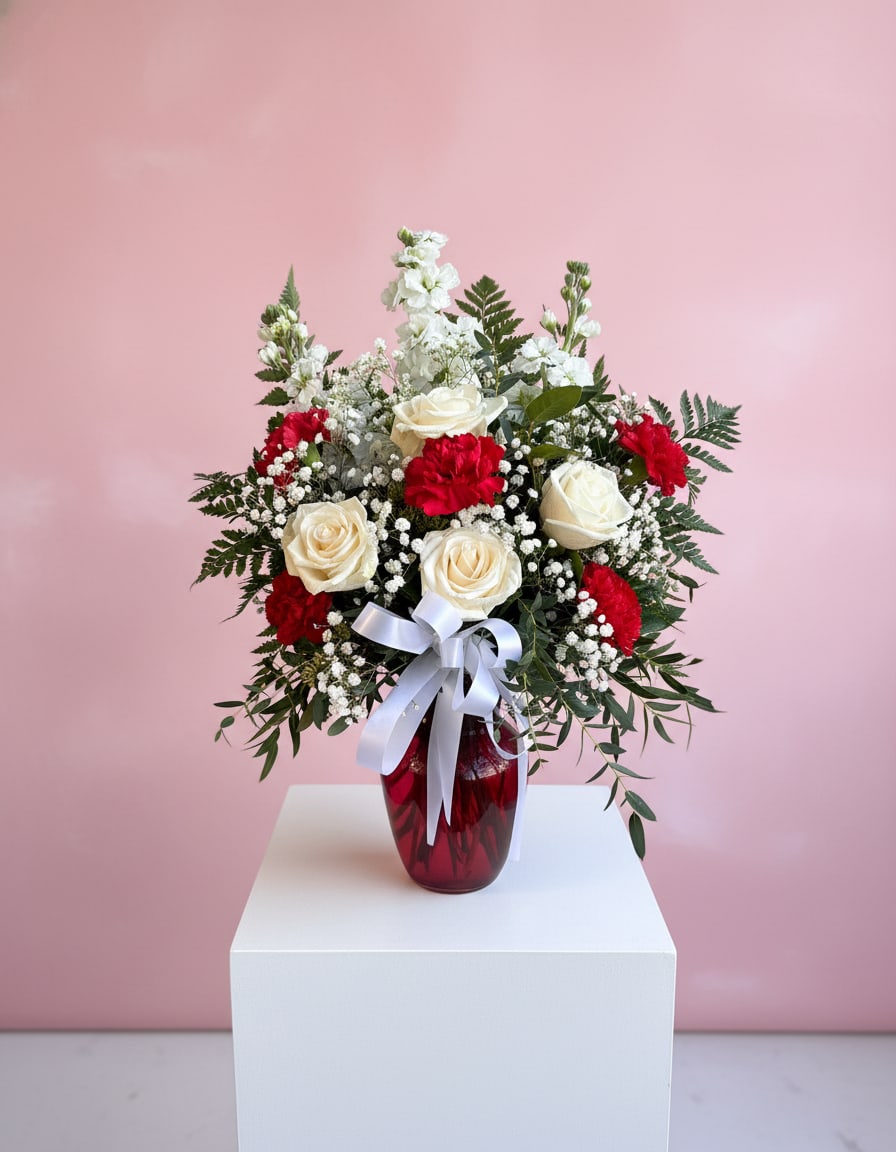 Red and white roses arranged in a red vase with a white ribbon