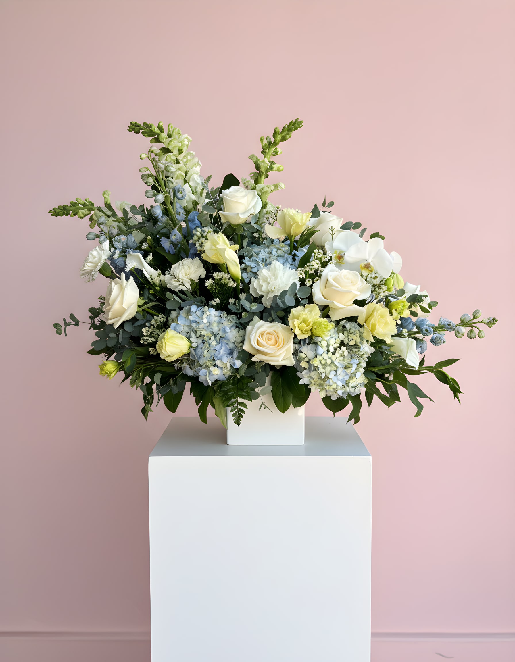 Large white and pale blue floral arrangement in a white vase