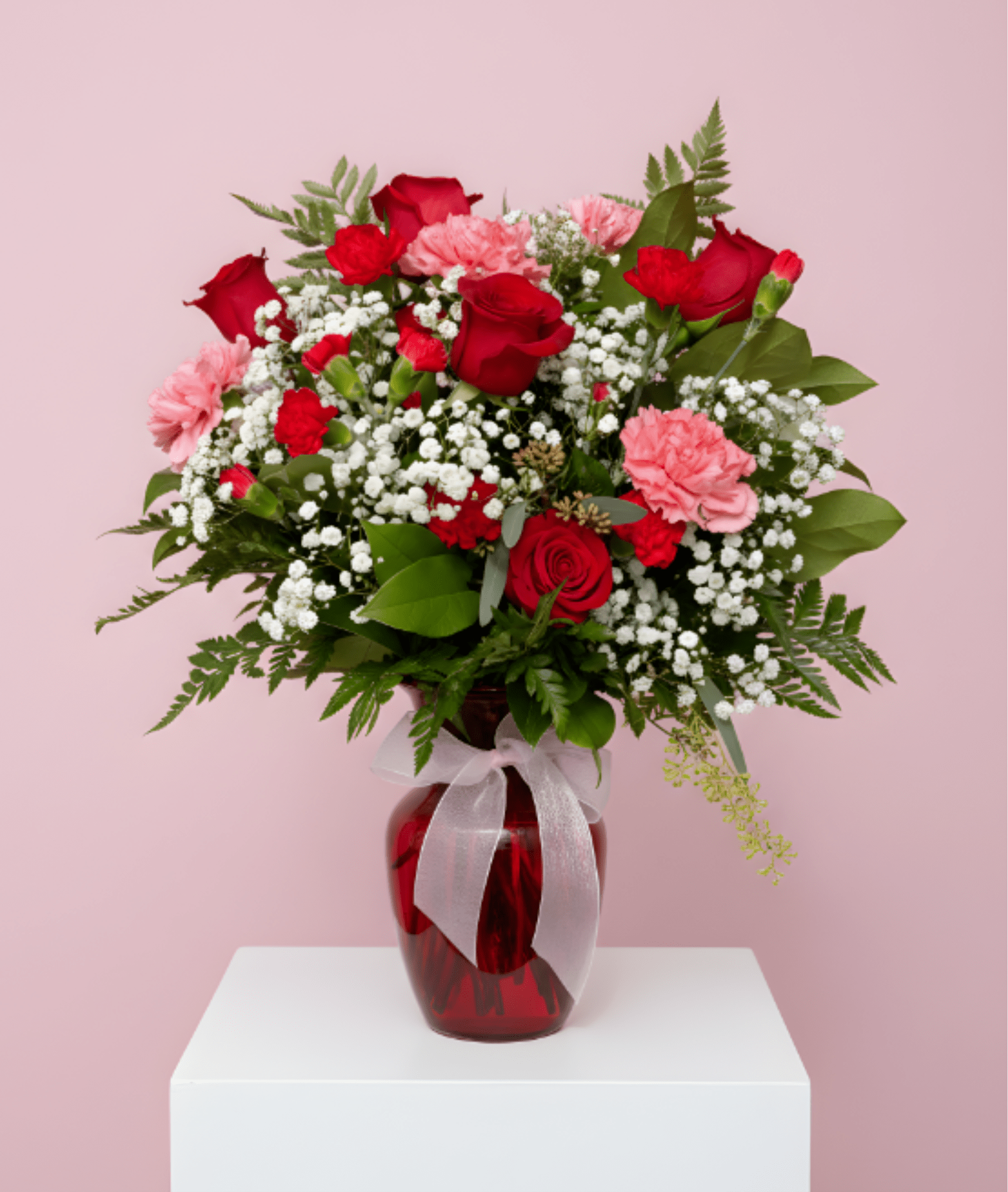 Red roses and pink carnations in a red glass vase with a white ribbon