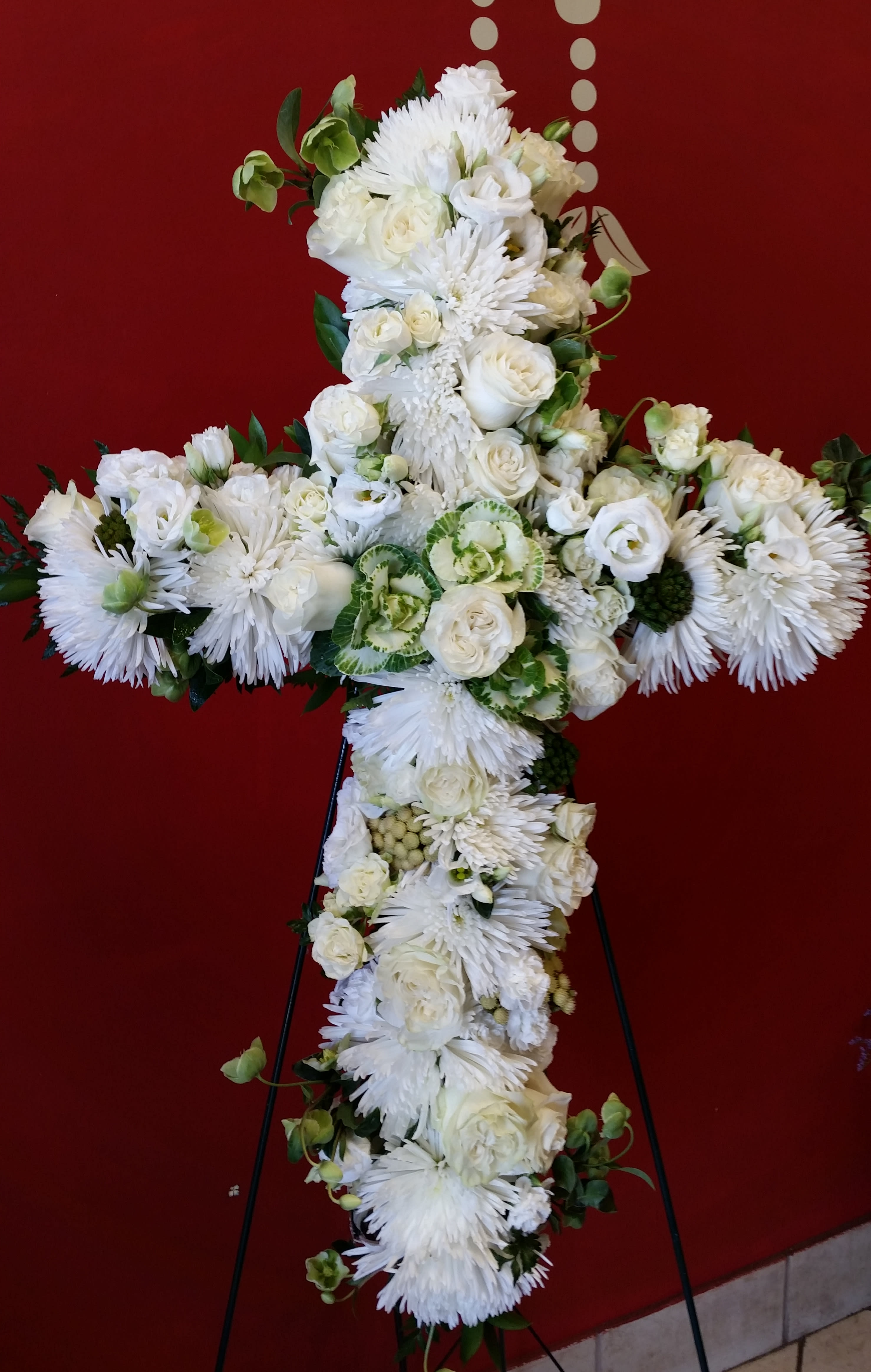 White floral cross on a stand against a red background