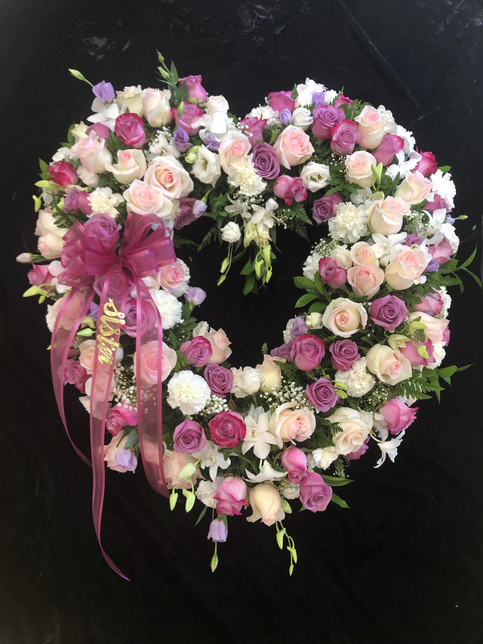 Heart-shaped floral wreath of pink, white, and purple roses with a ribbon bow