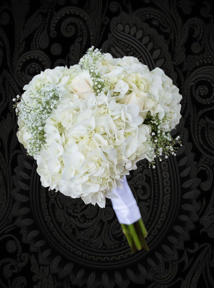 White bridal bouquet with hydrangeas and roses wrapped in white ribbon