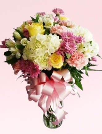 Bouquet of mixed pastel flowers with a pink ribbon in a glass vase
