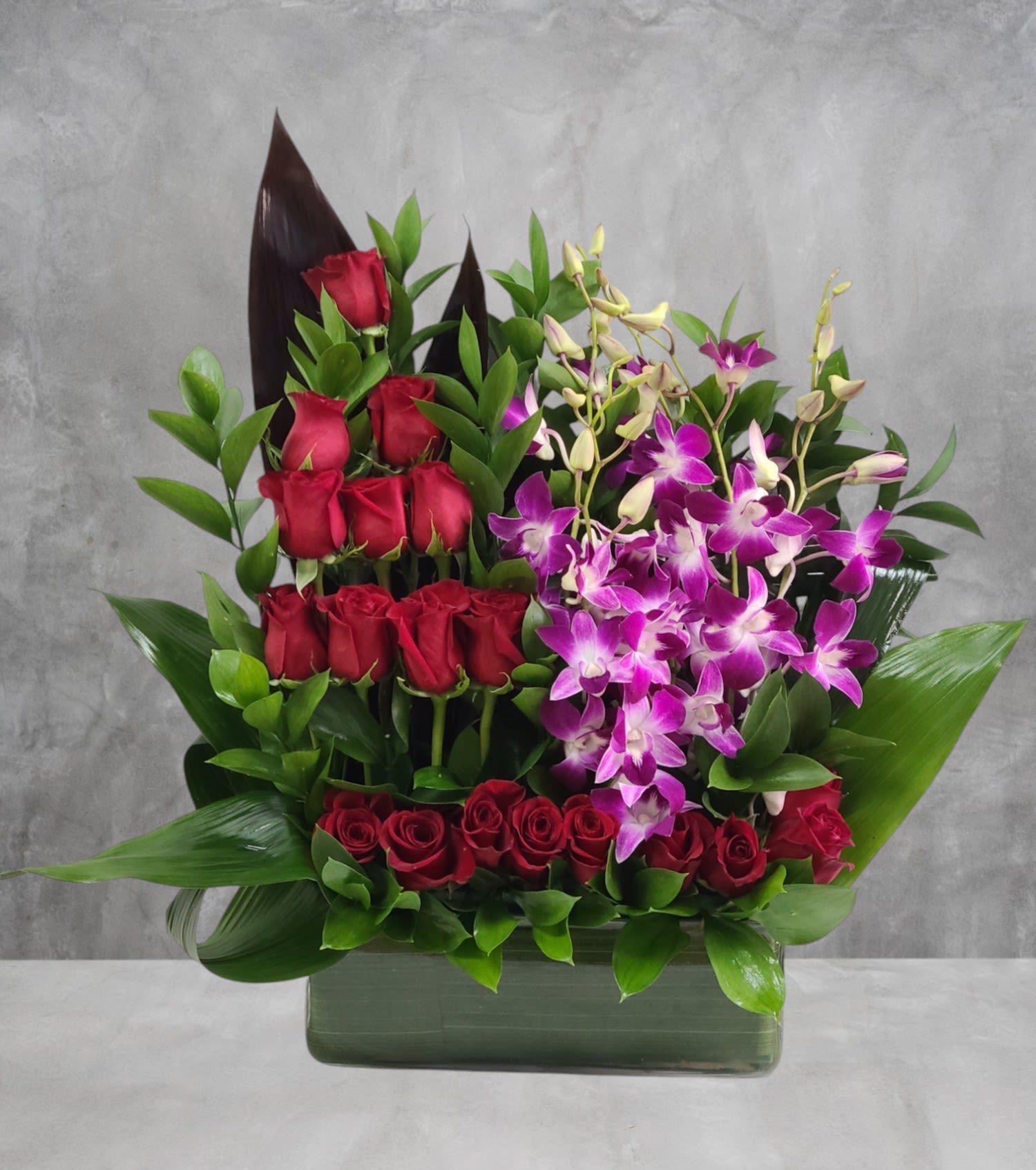 Red roses and purple orchids arranged in a rectangular vase
