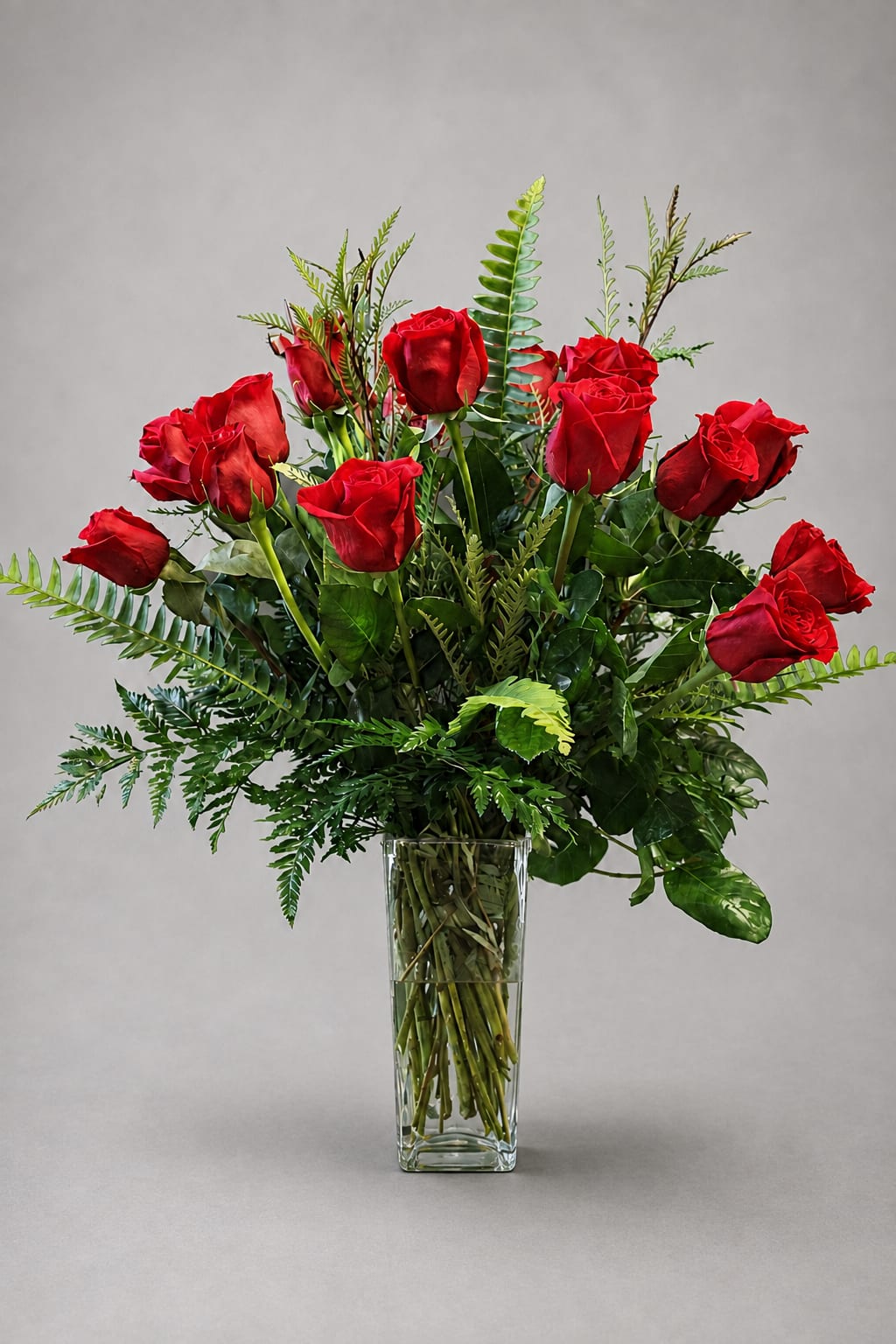 Red roses arranged in a clear glass vase with greenery
