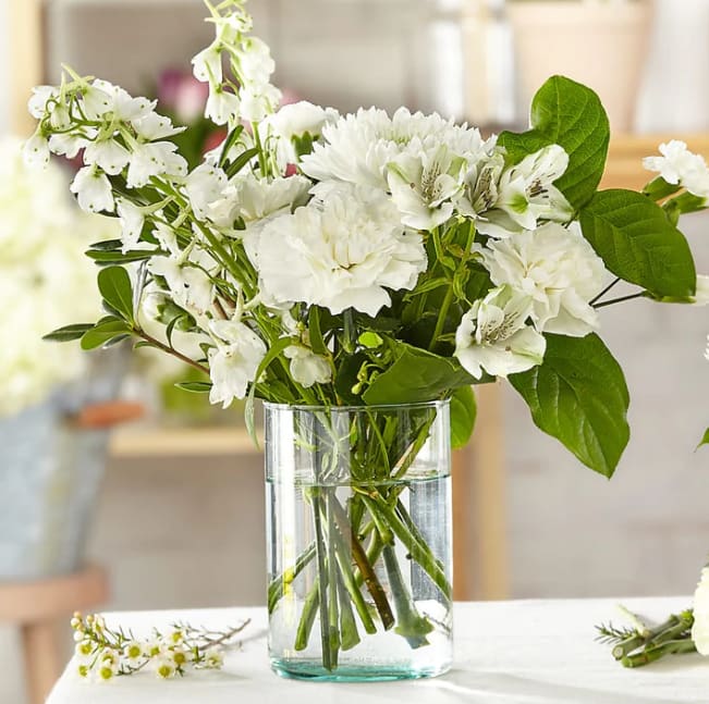 White flowers arranged in a clear glass vase with green leaves