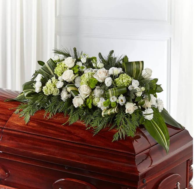 White and green floral casket spray on a polished wooden casket