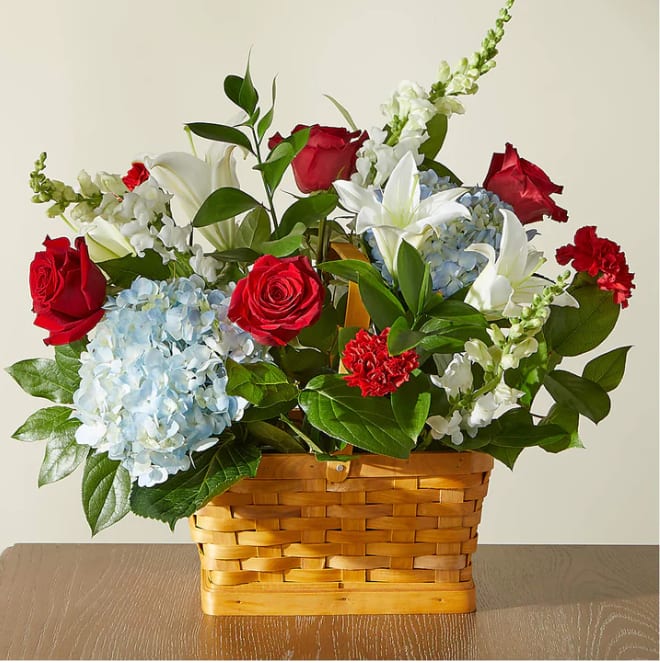 Basket arrangement of red roses, white lilies, and blue hydrangeas