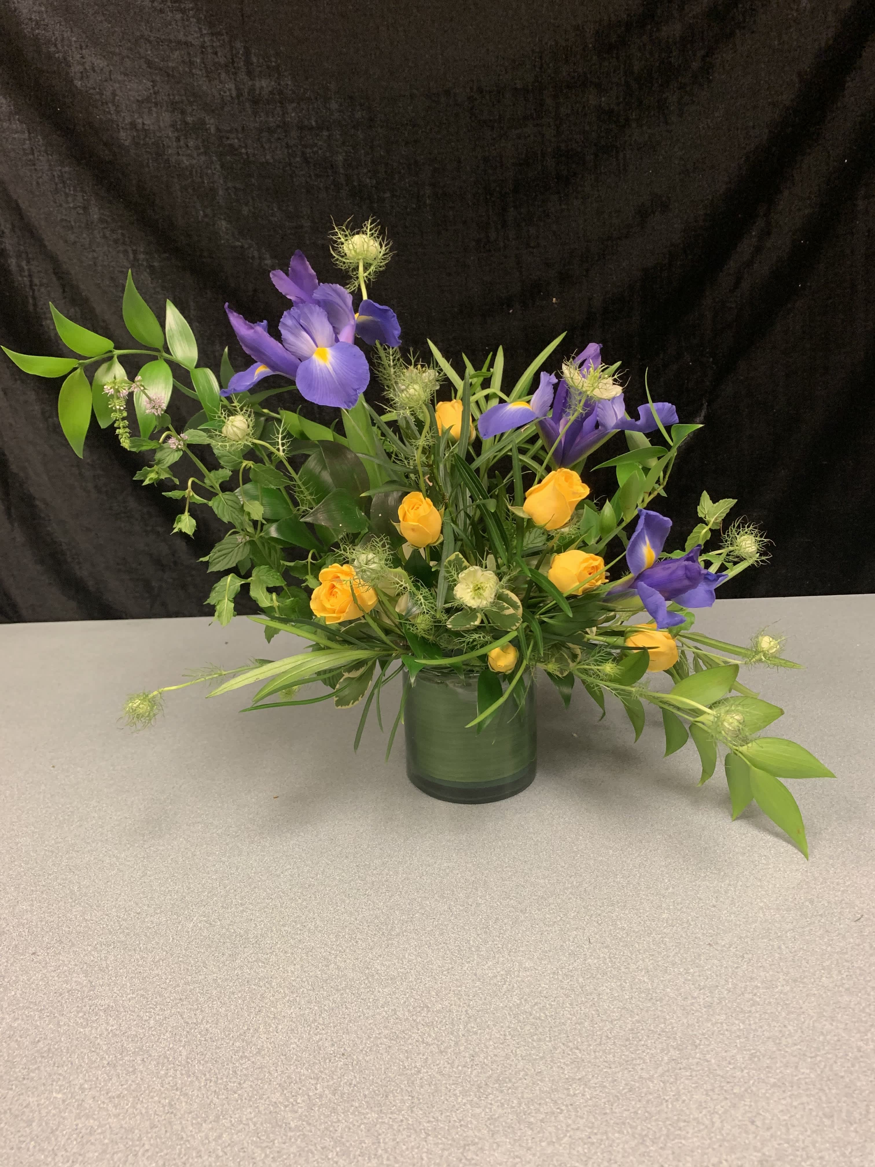 Purple iris and yellow roses arranged in a glass vase