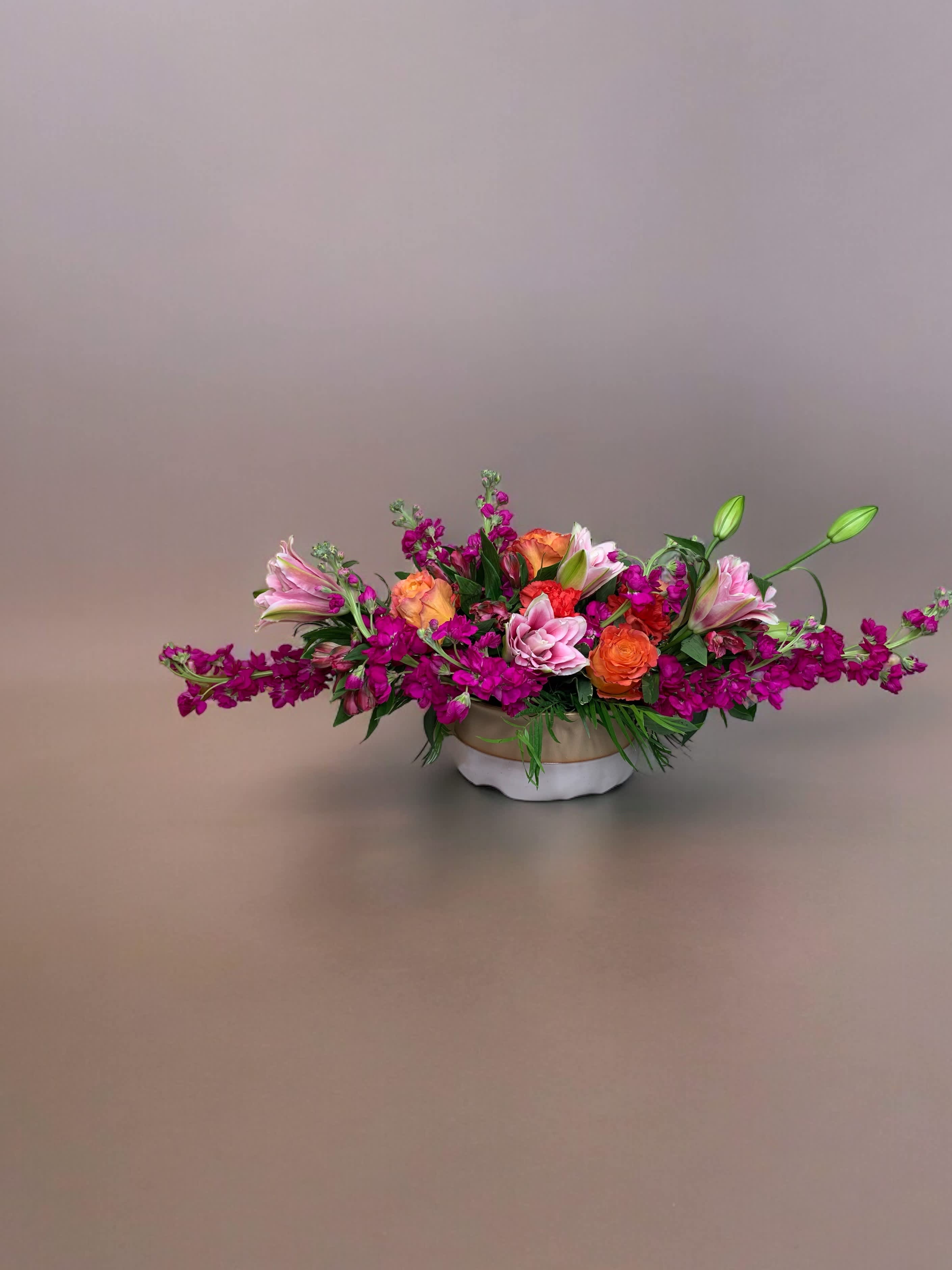 Low floral centerpiece with pink, orange, and magenta blooms in a white bowl vase