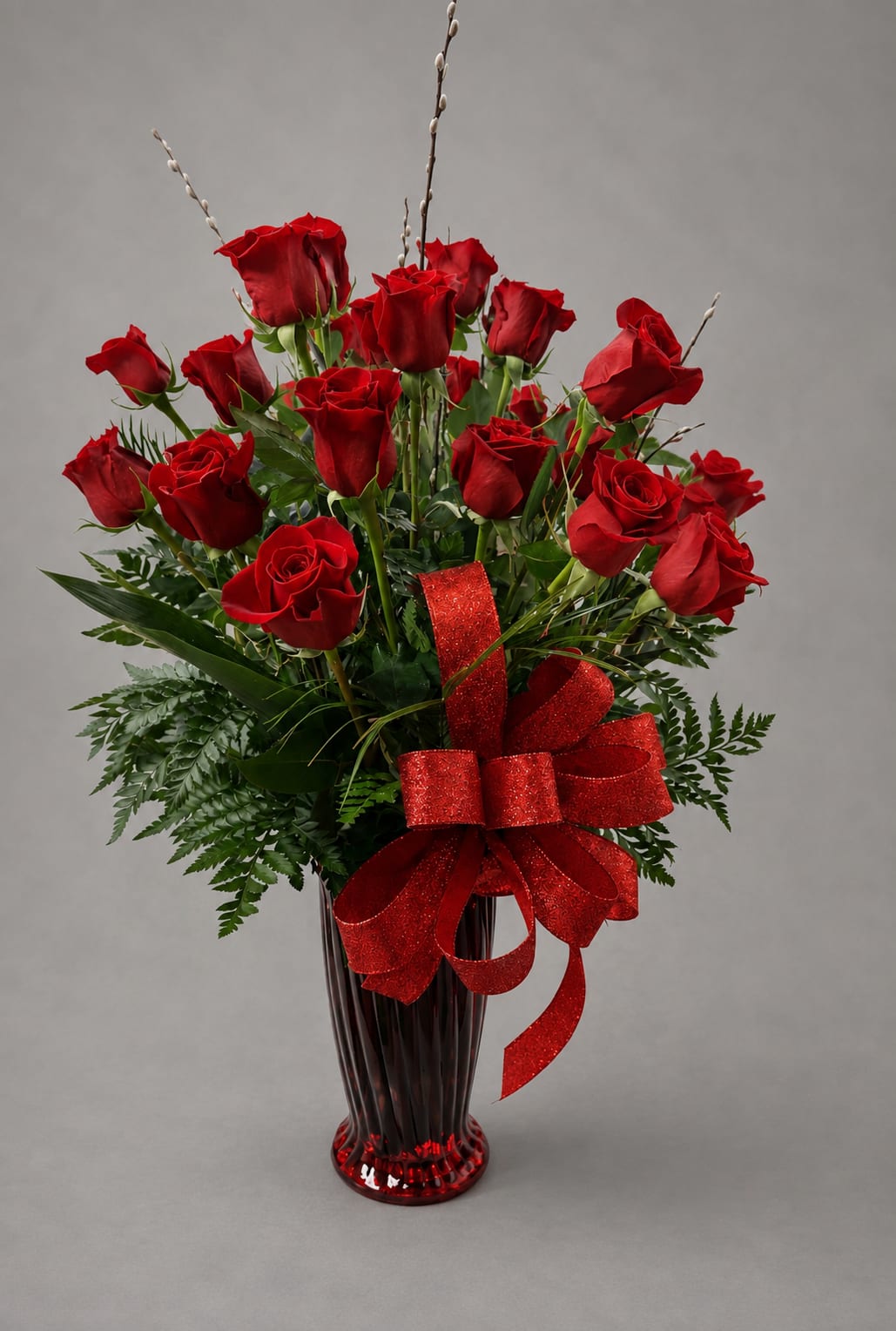 Red roses arranged in a tall red vase with a glittery red bow
