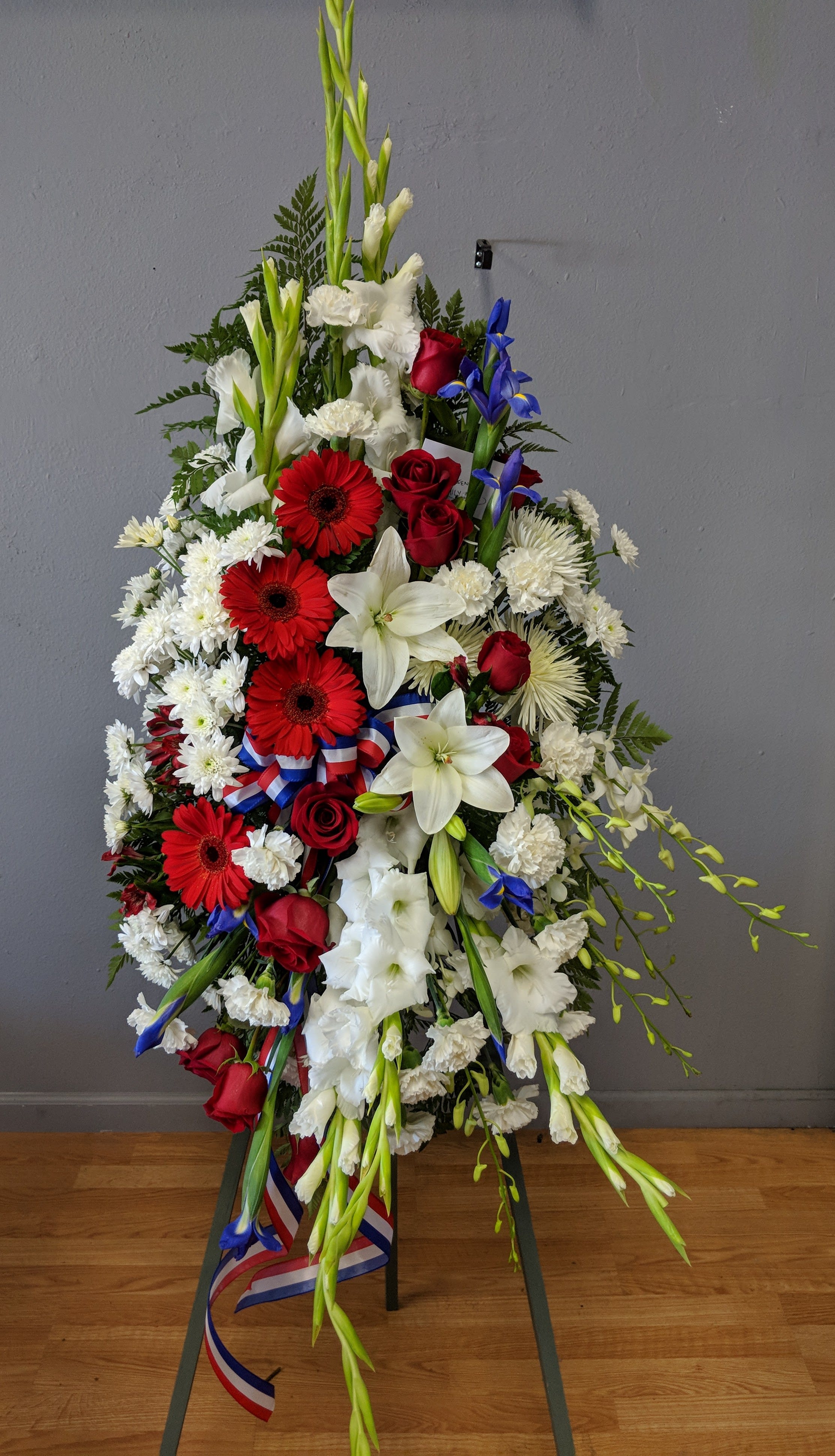 Standing floral spray with red, white, and blue flowers on a ribboned easel