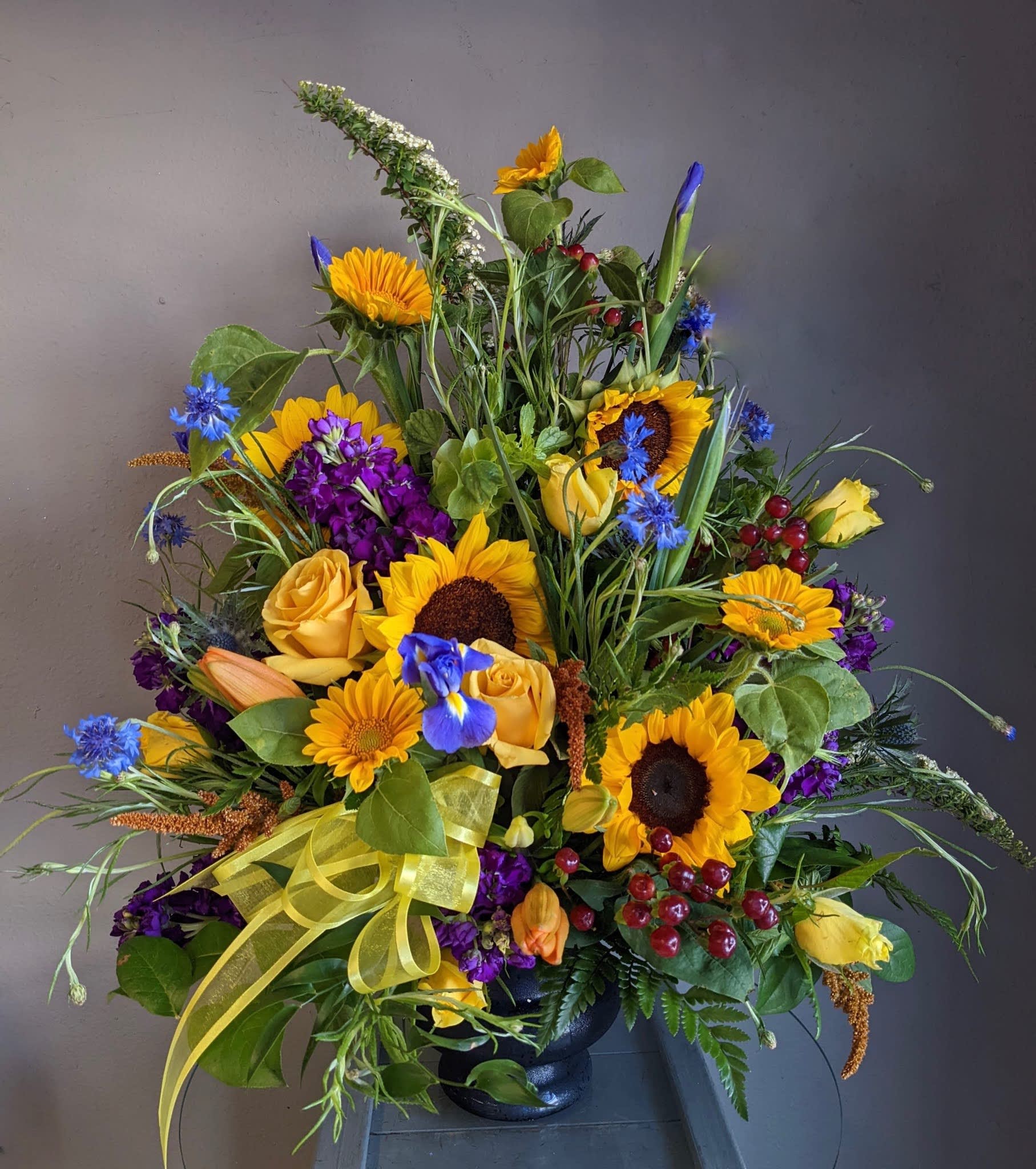 Large mixed bouquet with sunflowers, yellow roses, and purple flowers in a black vase
