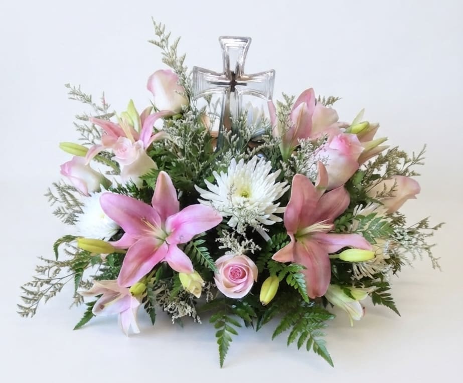 Pink lilies and white flowers arranged around a clear glass cross