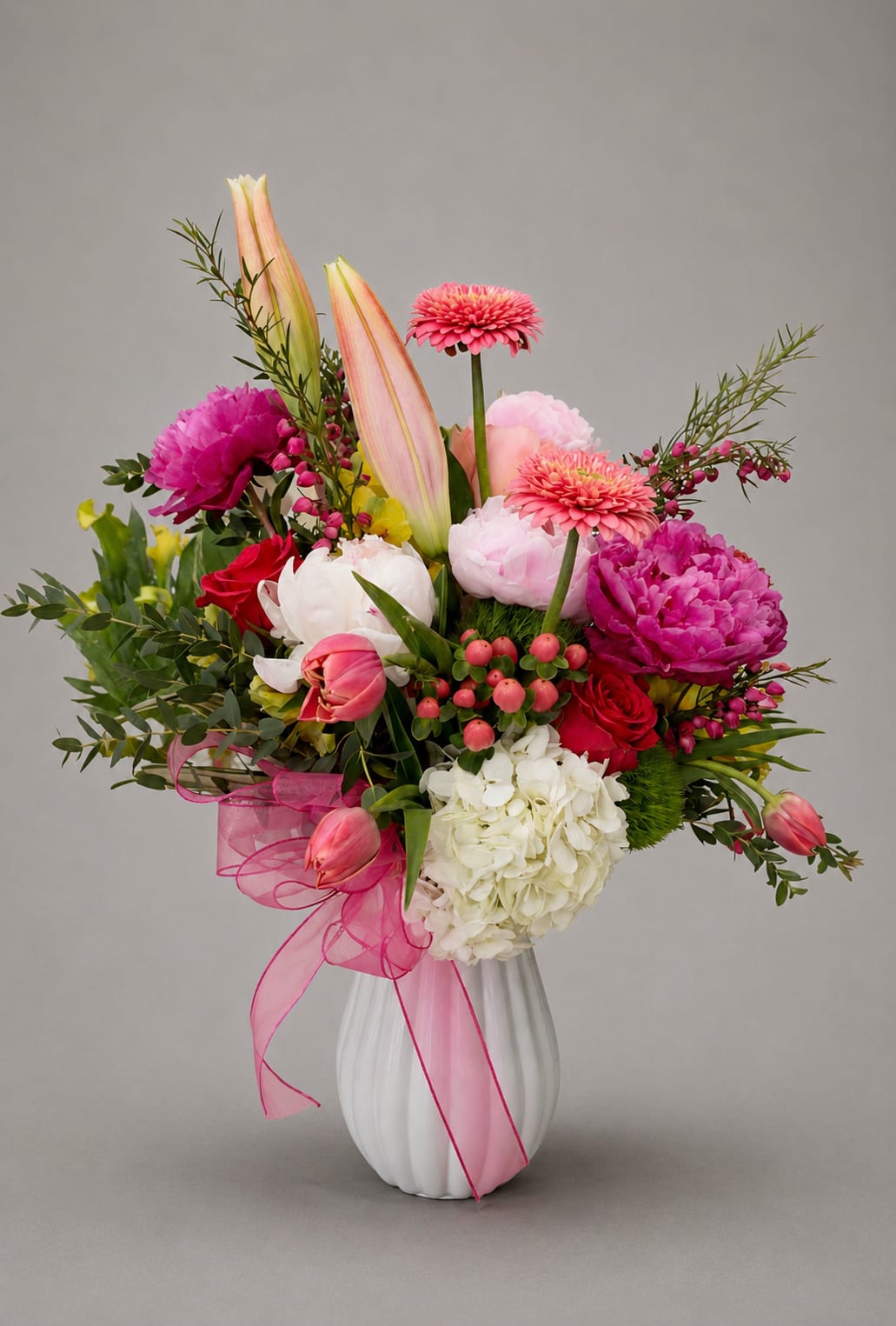 Pink and white mixed flower arrangement in a white vase with a pink ribbon