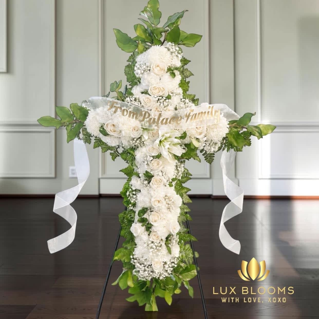 White floral cross arrangement with ribbon streamers and greenery