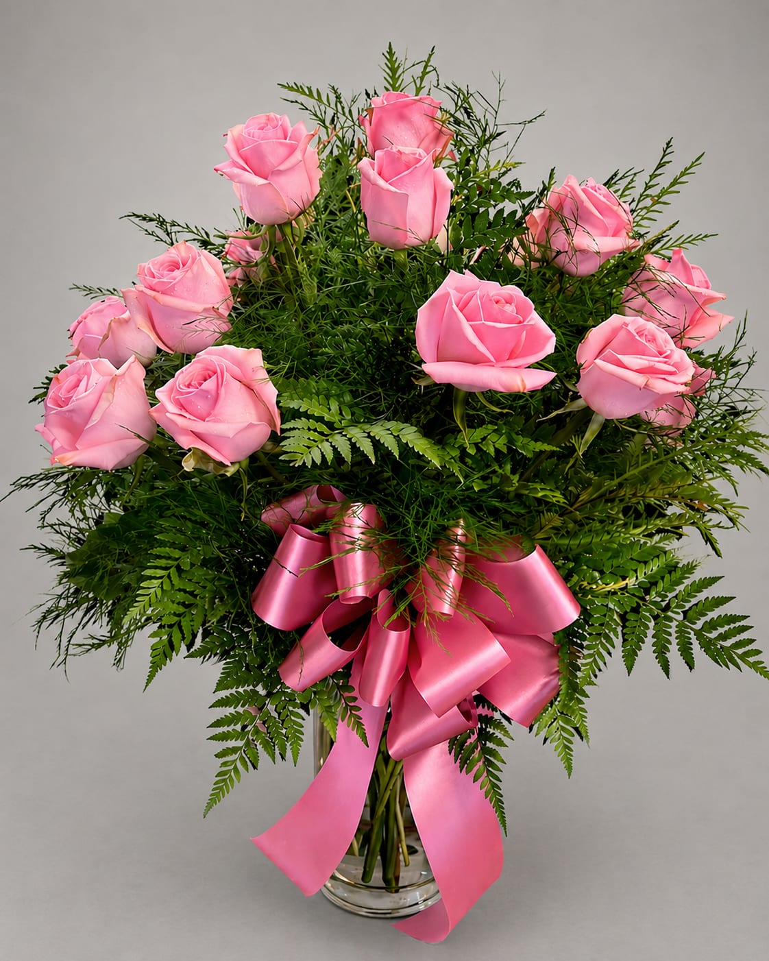 Pink roses arranged in a clear glass vase with a pink ribbon